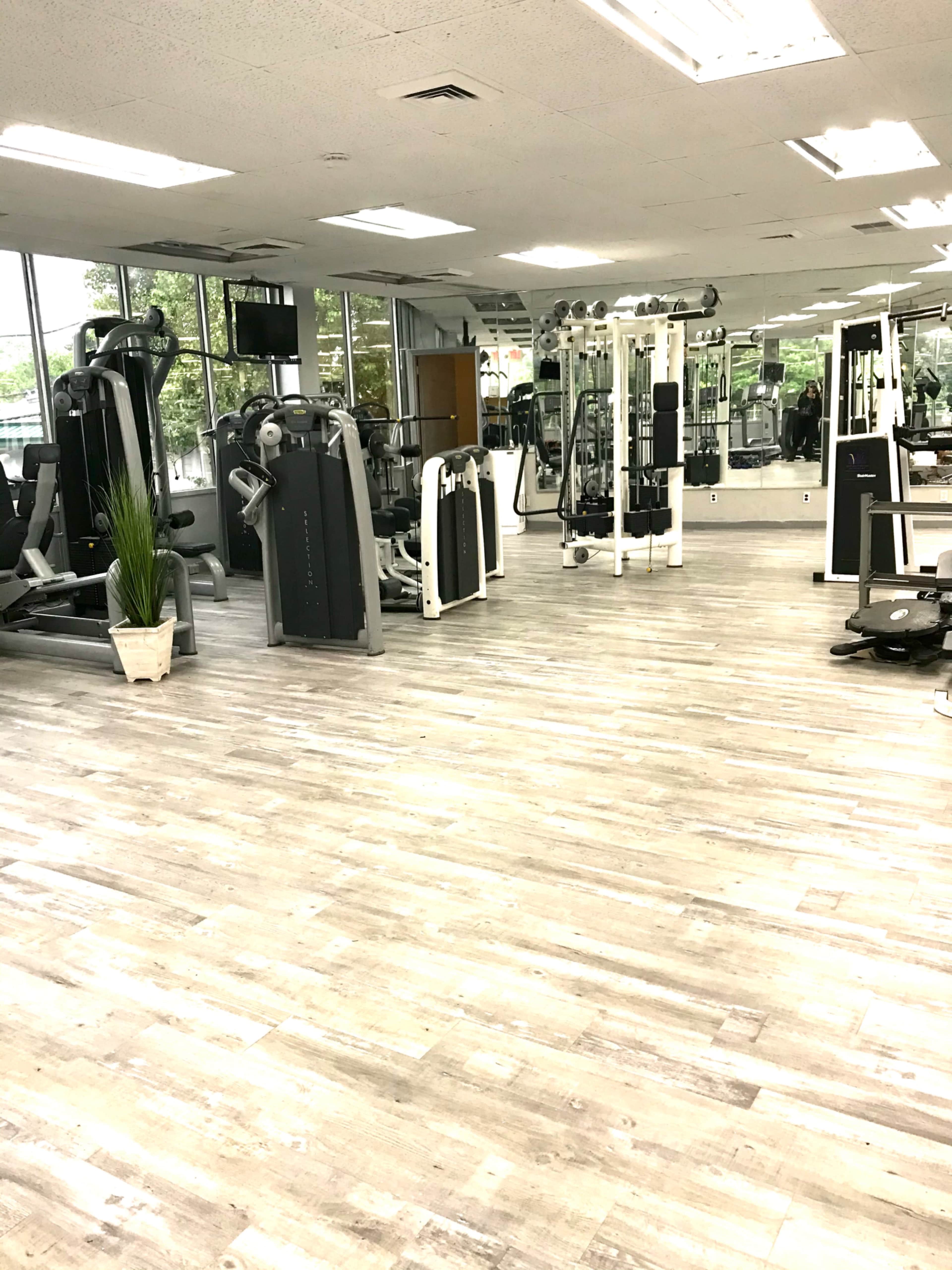 A spacious gym with various exercise equipment arranged neatly along the walls and a large mirror reflecting the interior.