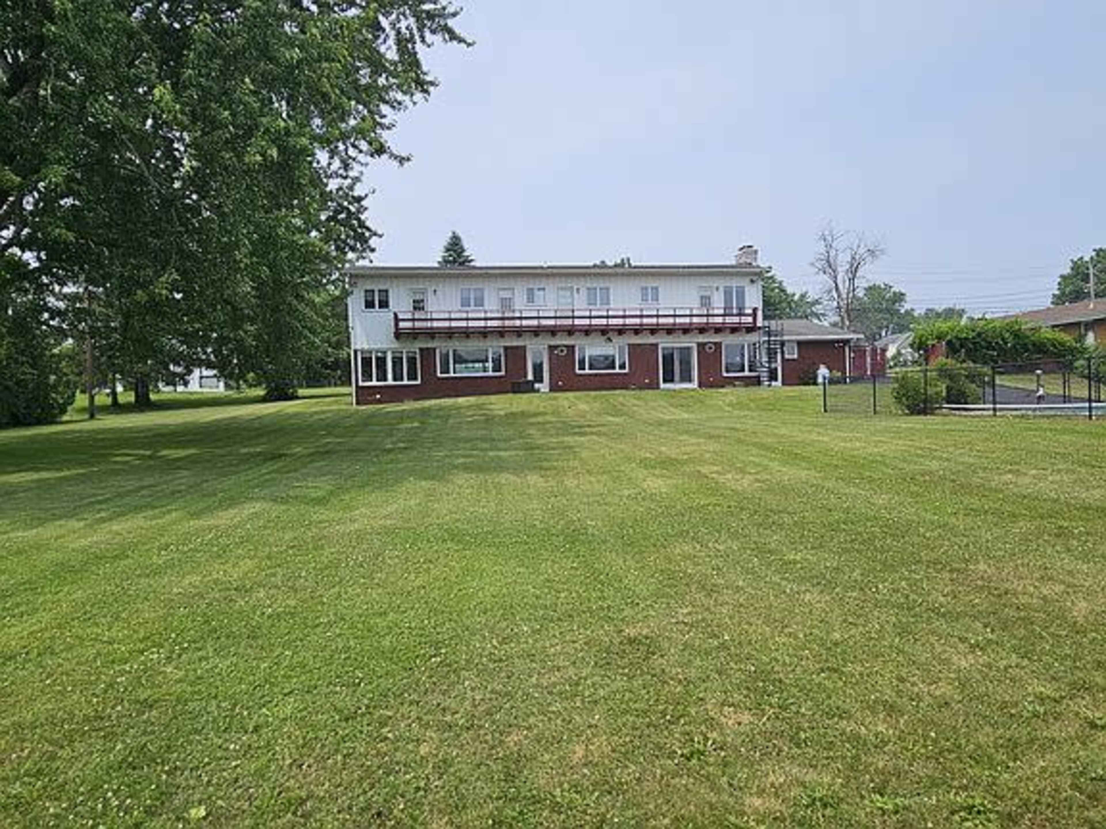 A two-story building with a red brick lower level and white upper level is situated on a large, green lawn.