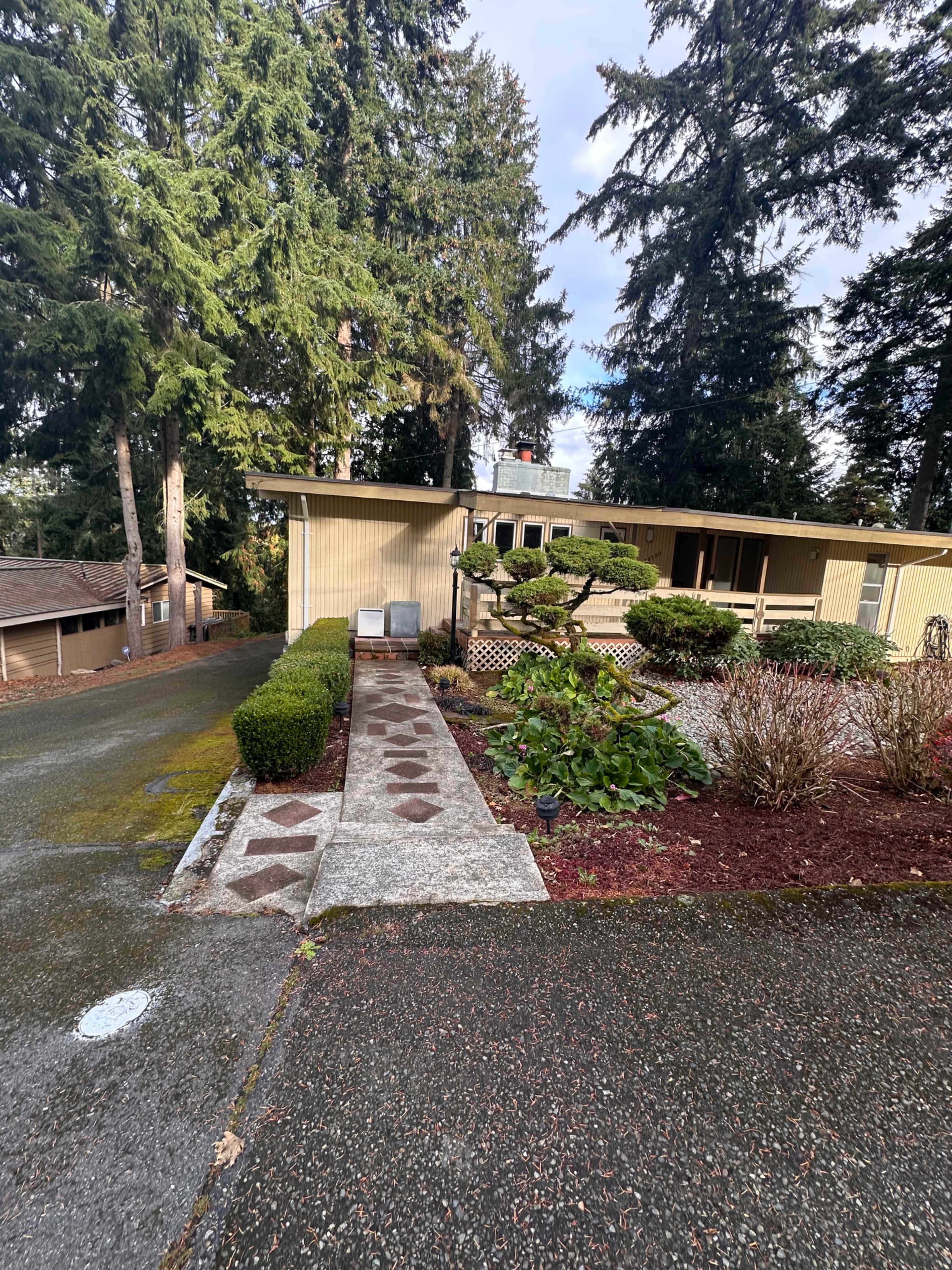 A driveway leads up to a house with a front porch, bordered by landscaped greenery and trees.