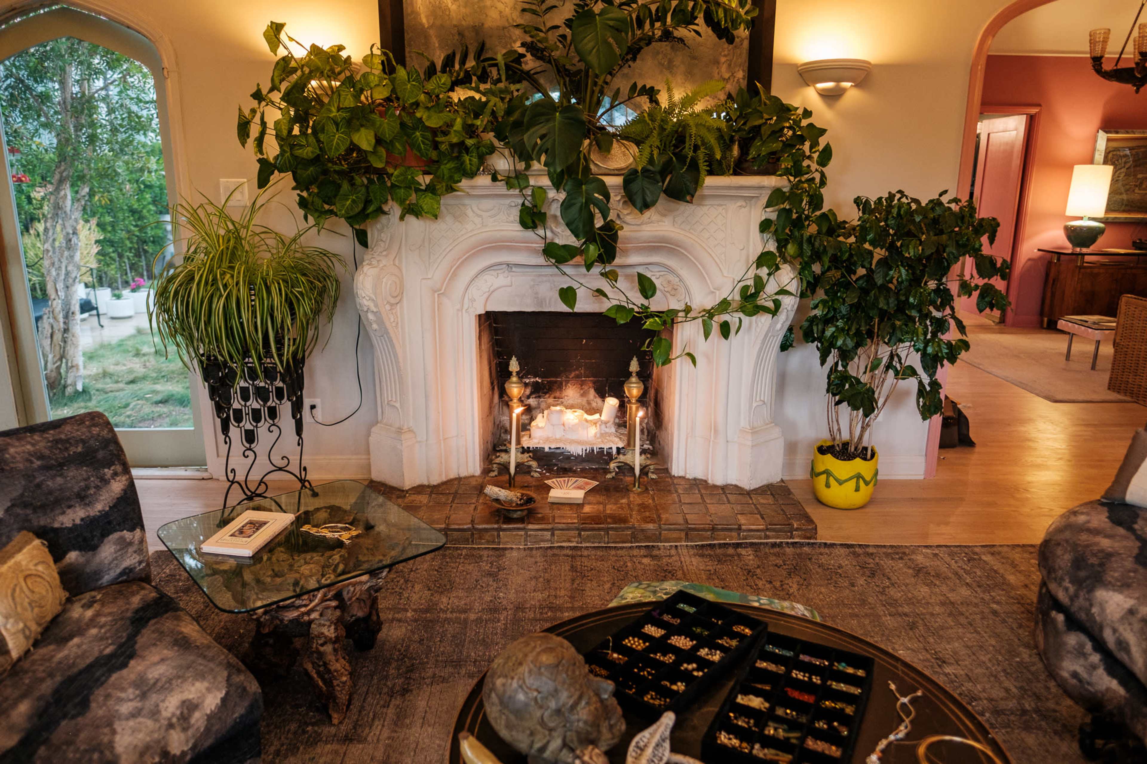 A cozy living room features a fireplace adorned with greenery and a coffee table displaying various jewelry pieces.