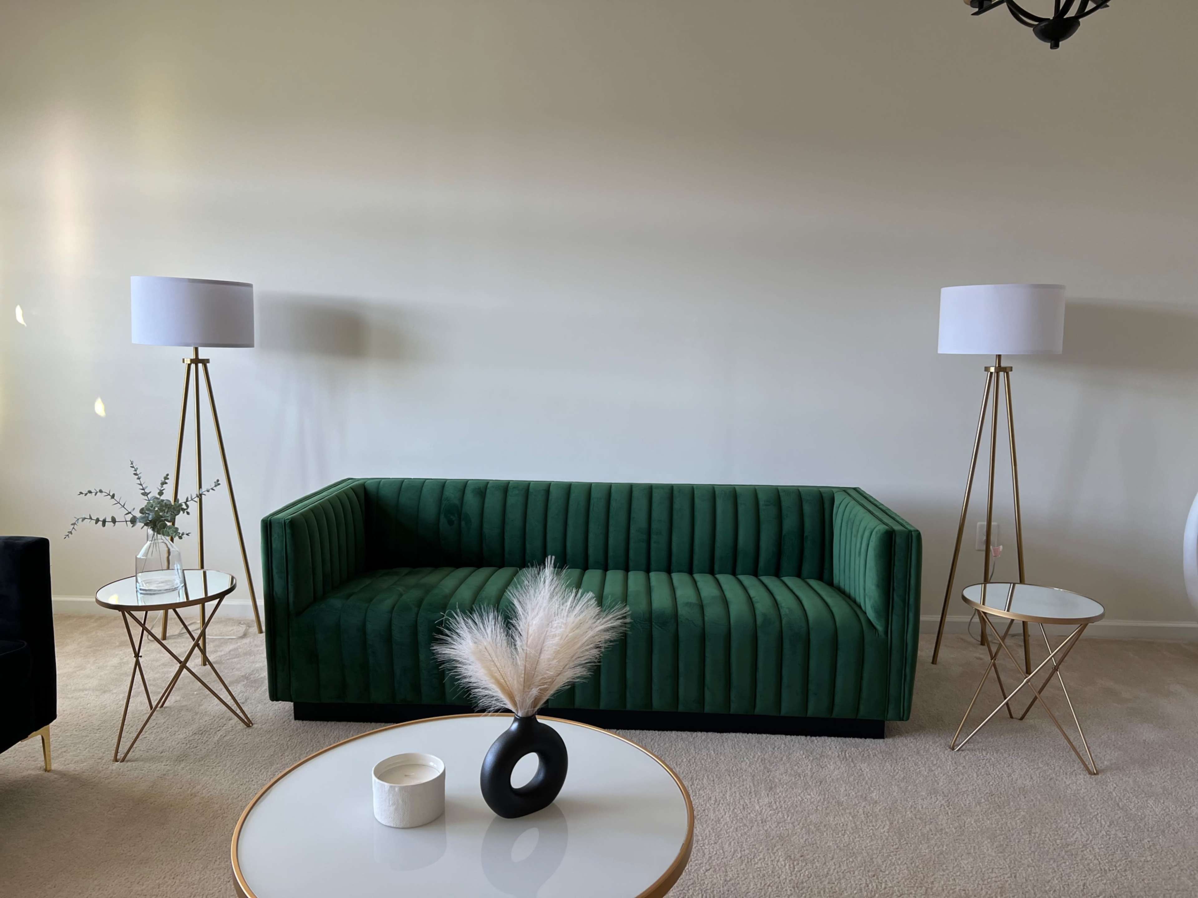 A green upholstered sofa with vertical stripes, flanked by two floor lamps and two circular side tables, all set against a light-colored wall.
