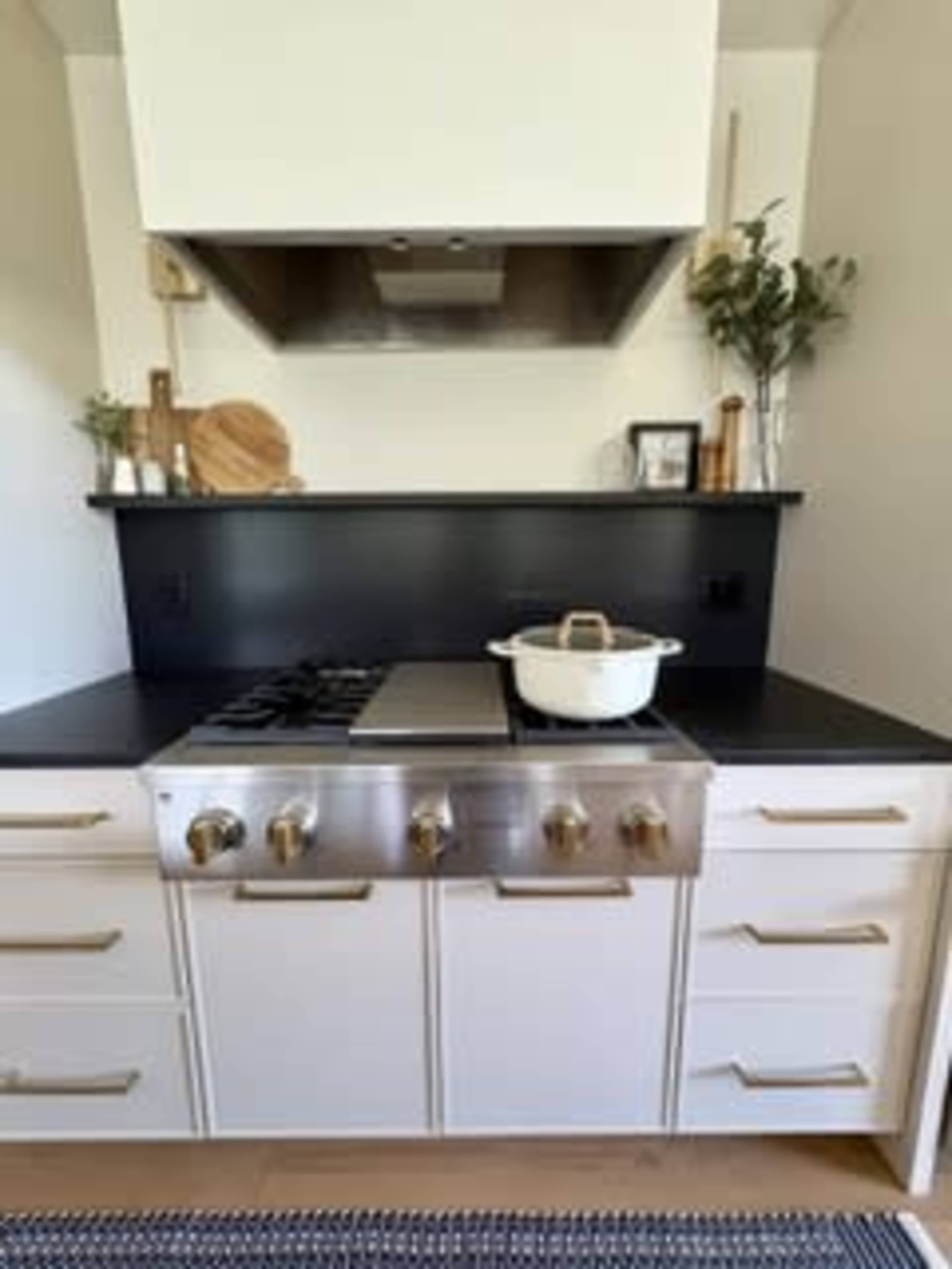 The image shows a modern kitchen featuring a stainless steel gas range, a white cooking pot on top, and a minimalistic black and white color scheme.