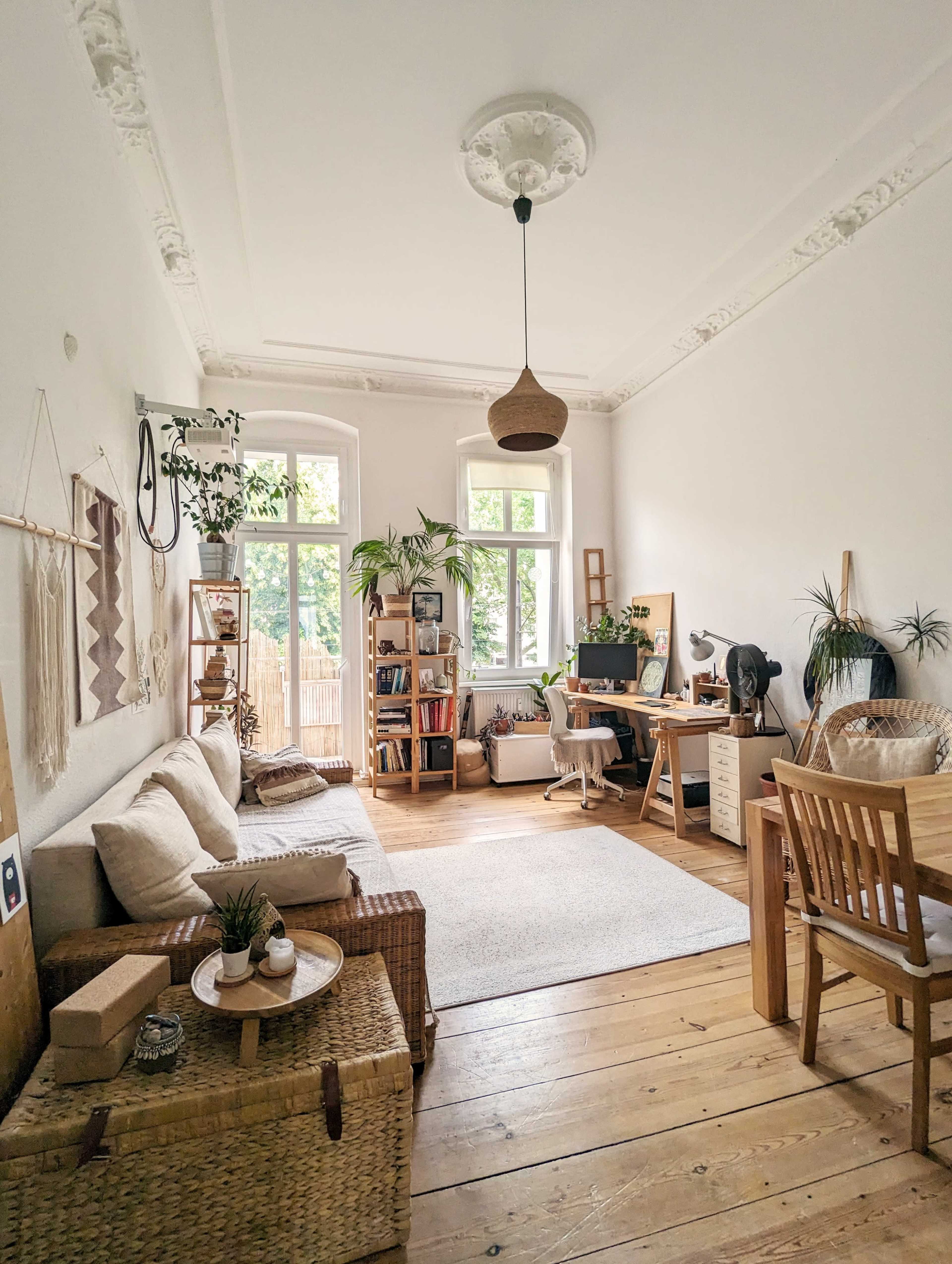 A bright, airy living space featuring a cozy seating area, a desk, plants, and wooden furniture.