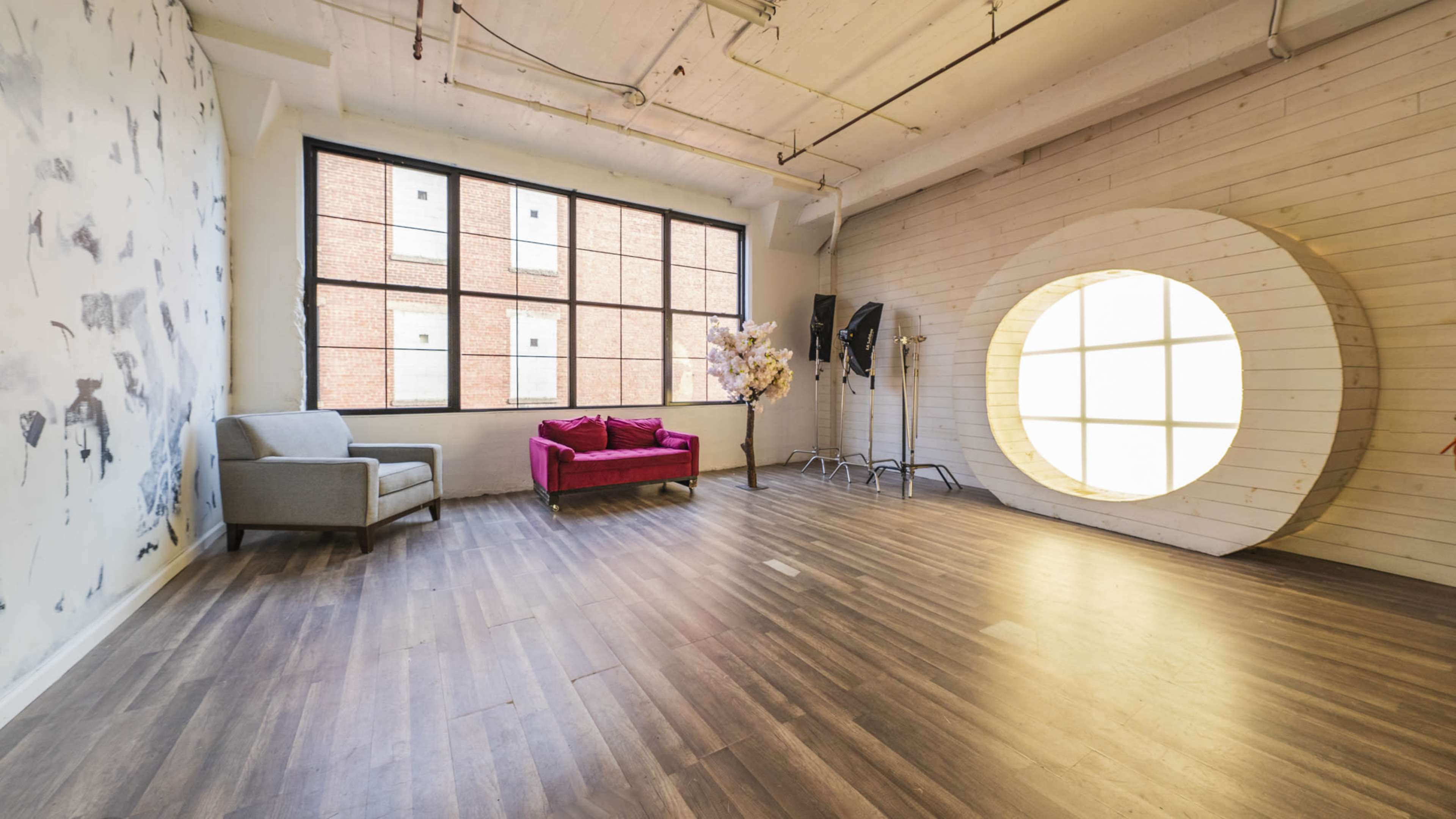 A spacious room with large windows, a pink sofa, and a round, wooden installation on one wall.