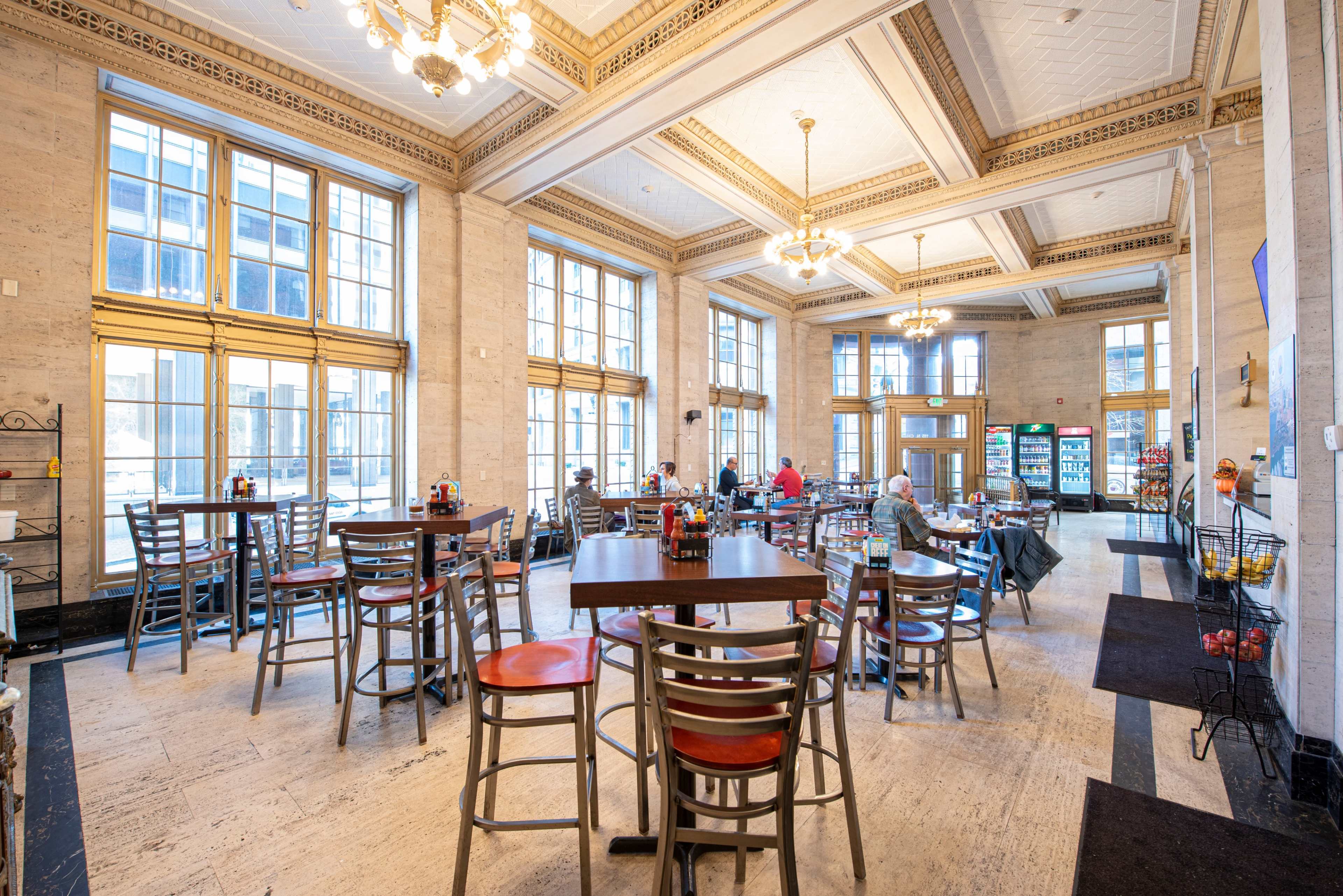 A spacious café with high ceilings, large windows, and several tall tables and chairs arranged throughout the room.