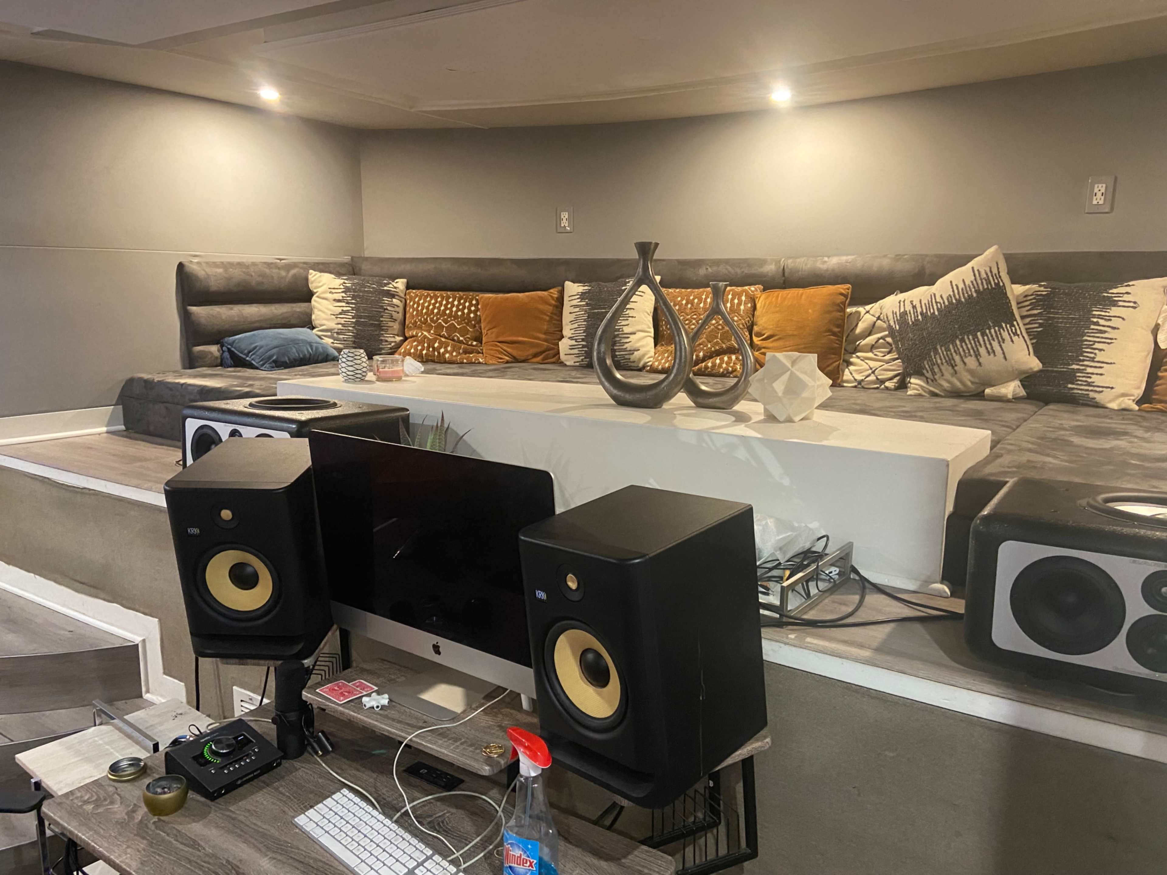 A modern studio space featuring a seating area with cushions and decorative items, alongside a desk equipped with audio speakers and a computer setup.