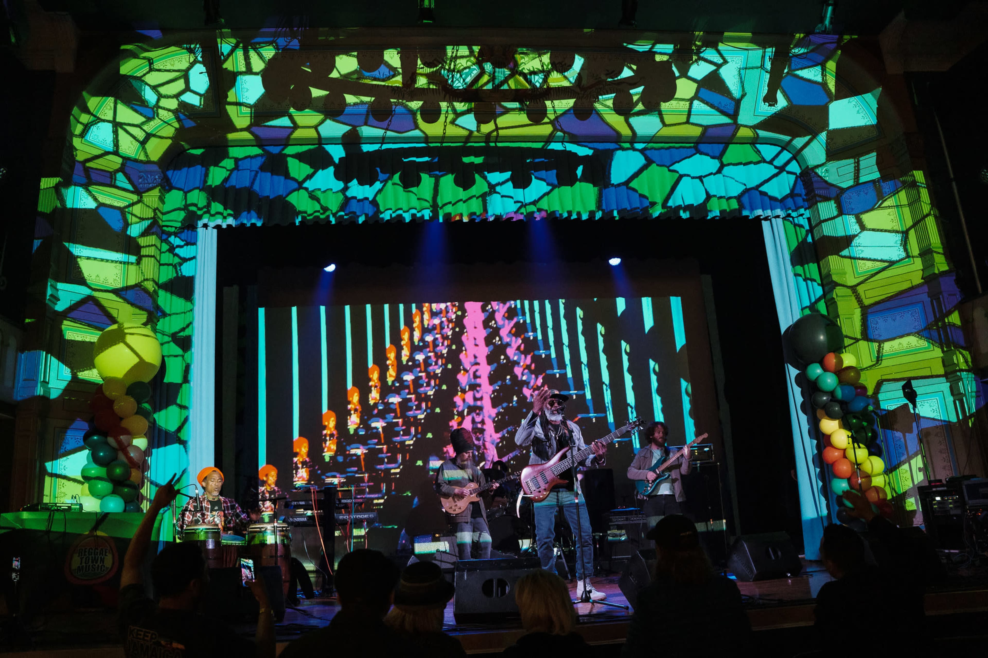 A live band performs on stage with colorful projections and patterned lighting surrounding them.
