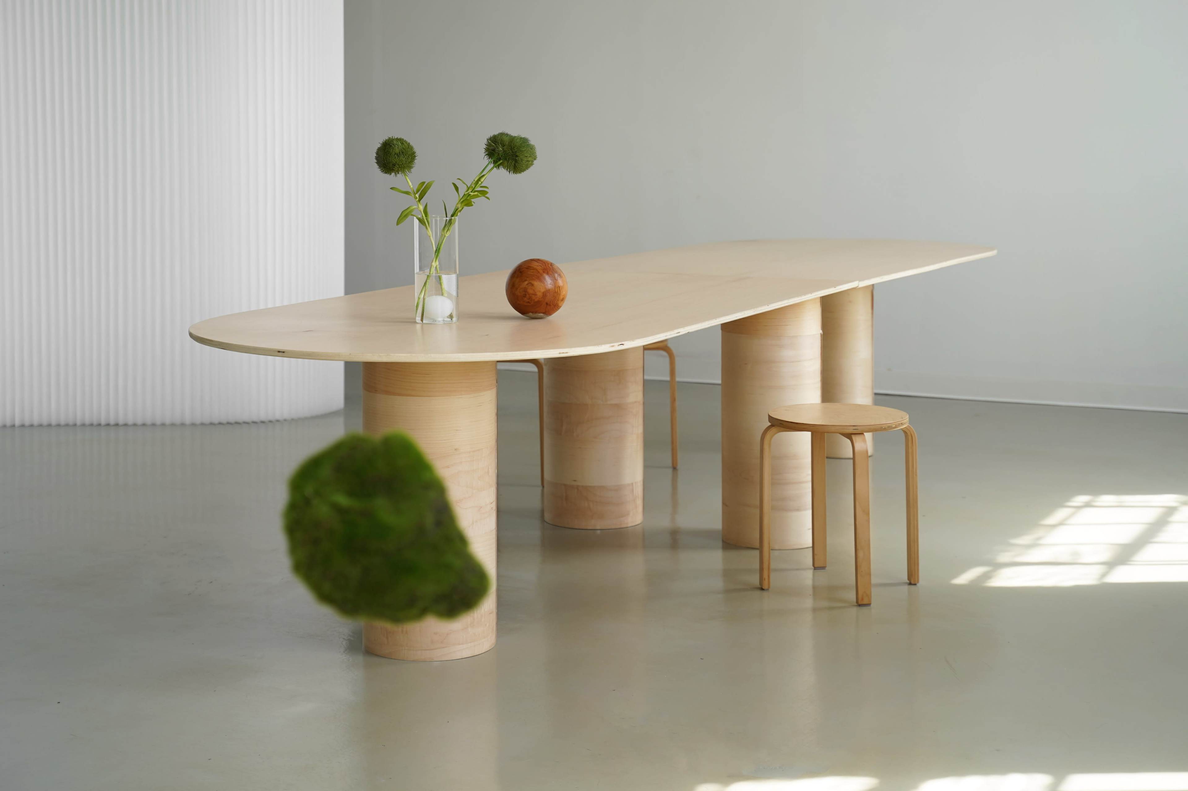 A modern wooden dining table with cylindrical bases is showcased alongside a chair and decorative elements like a vase and a round wooden object.