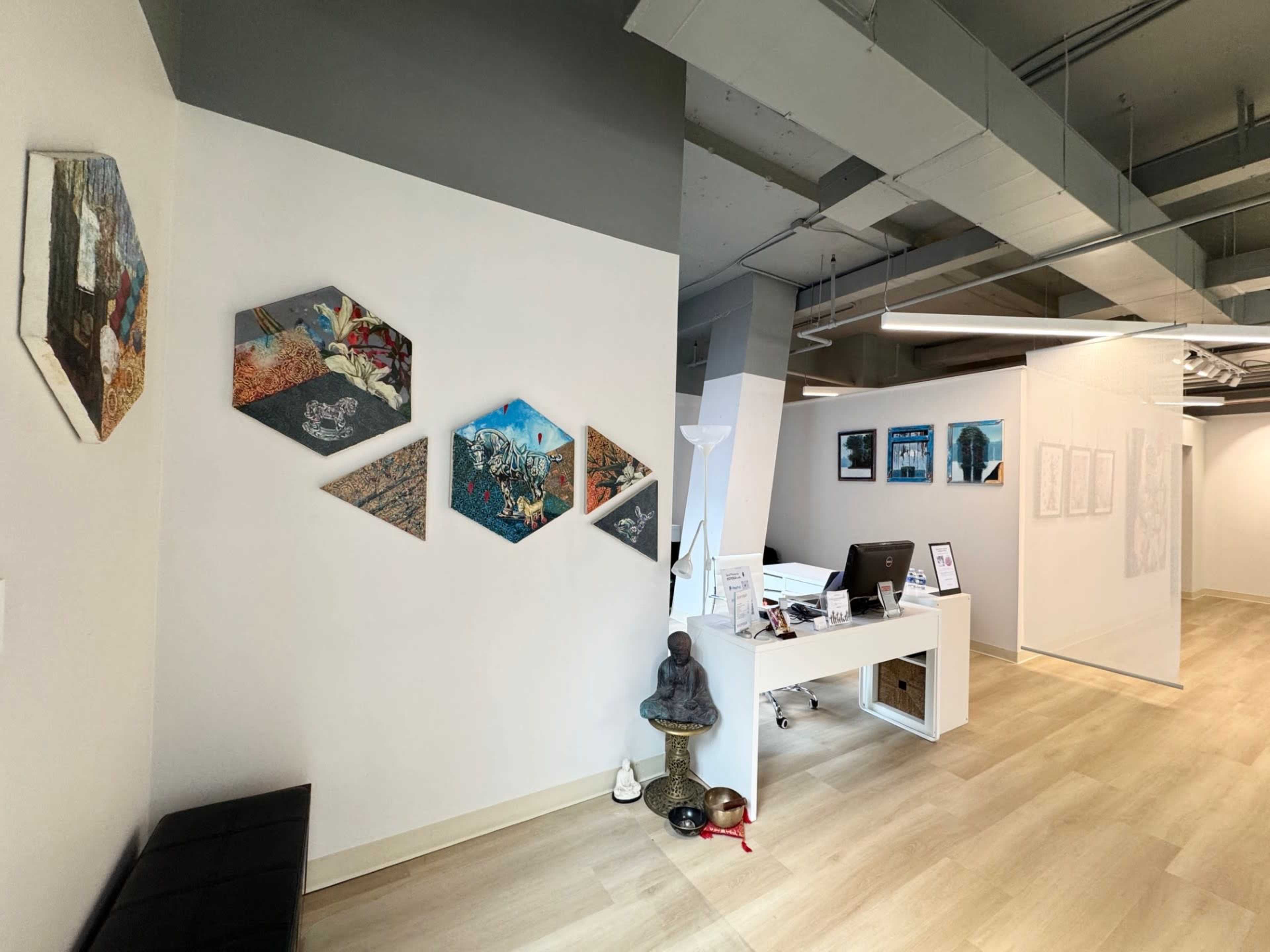 The image shows a modern office space with a reception desk, decorated walls featuring hexagonal art pieces, and a statue in a corner.