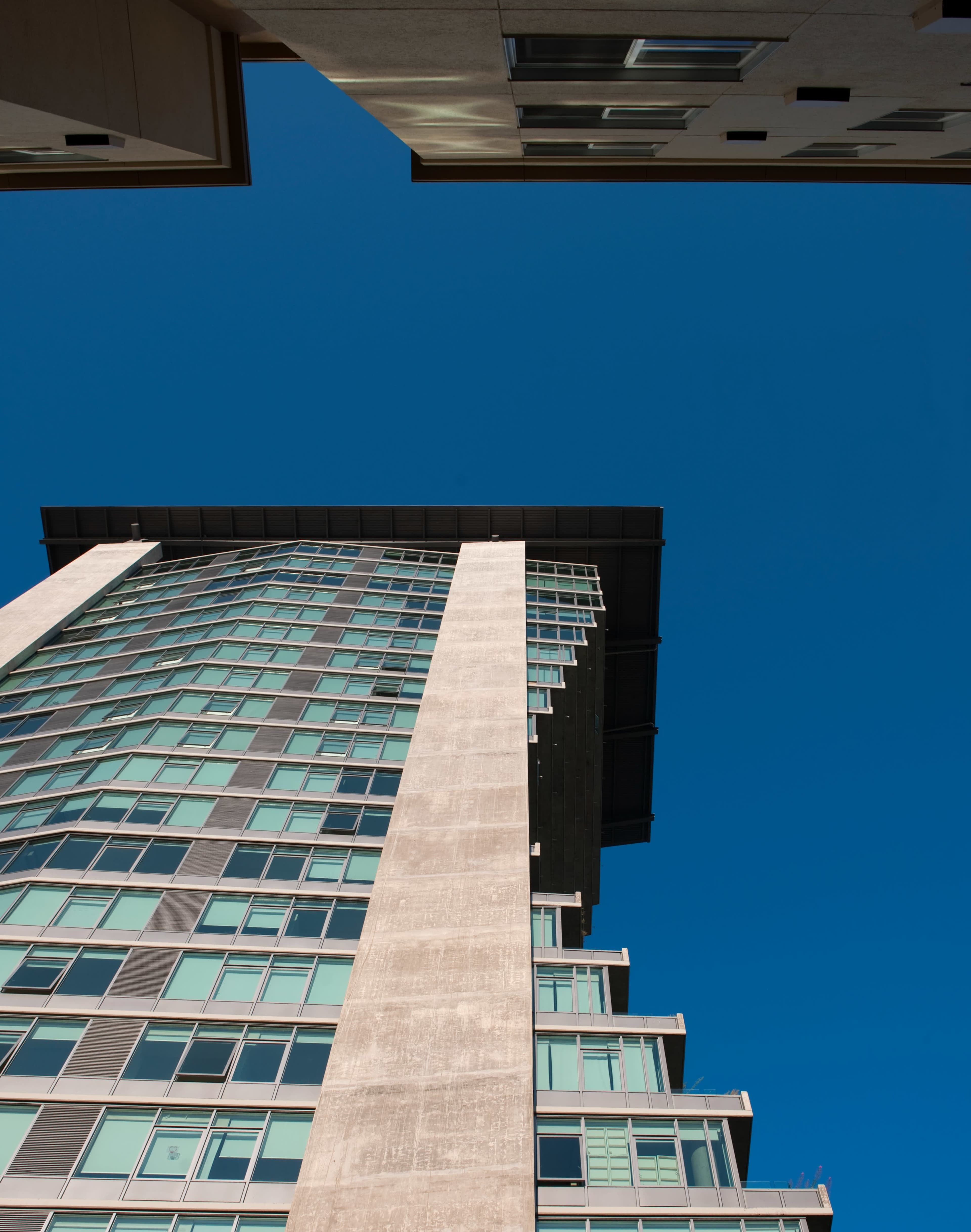 A tall modern building with large glass windows against a clear blue sky, viewed from the ground looking up.