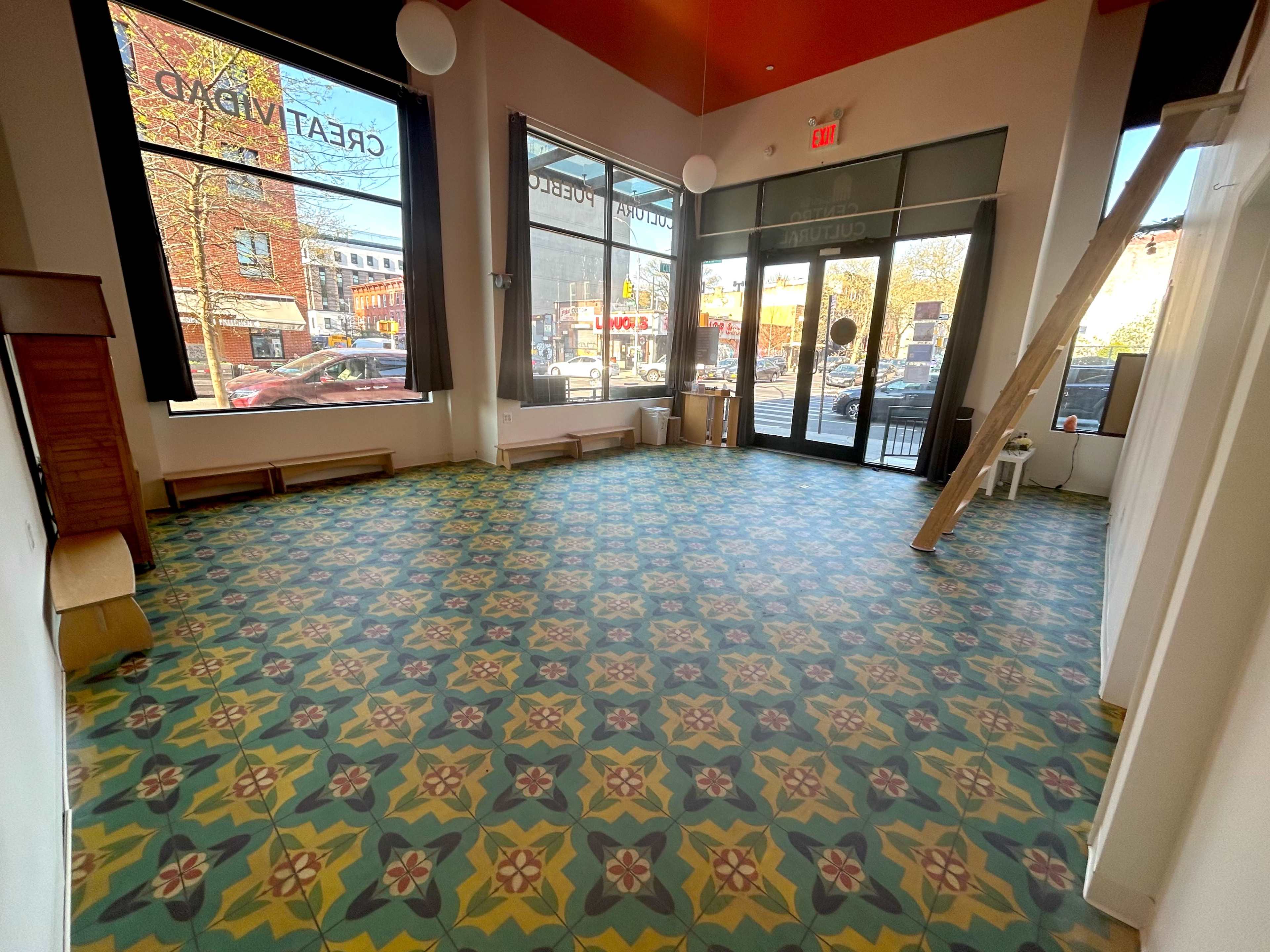 A spacious, empty room with patterned tiled flooring and large windows facing a street outside.