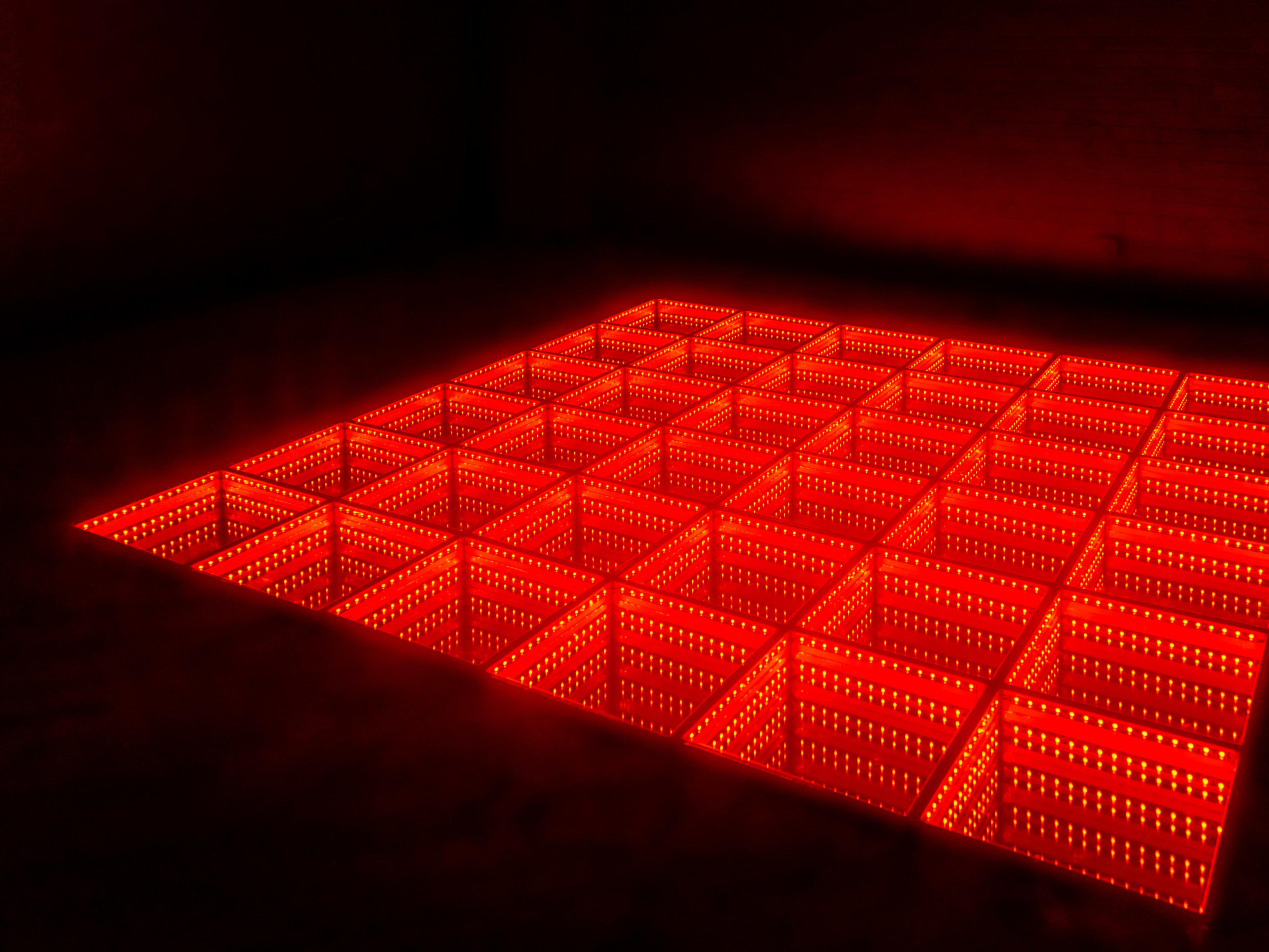 A grid of illuminated red squares is arranged on a dark floor, creating a glowing pattern.