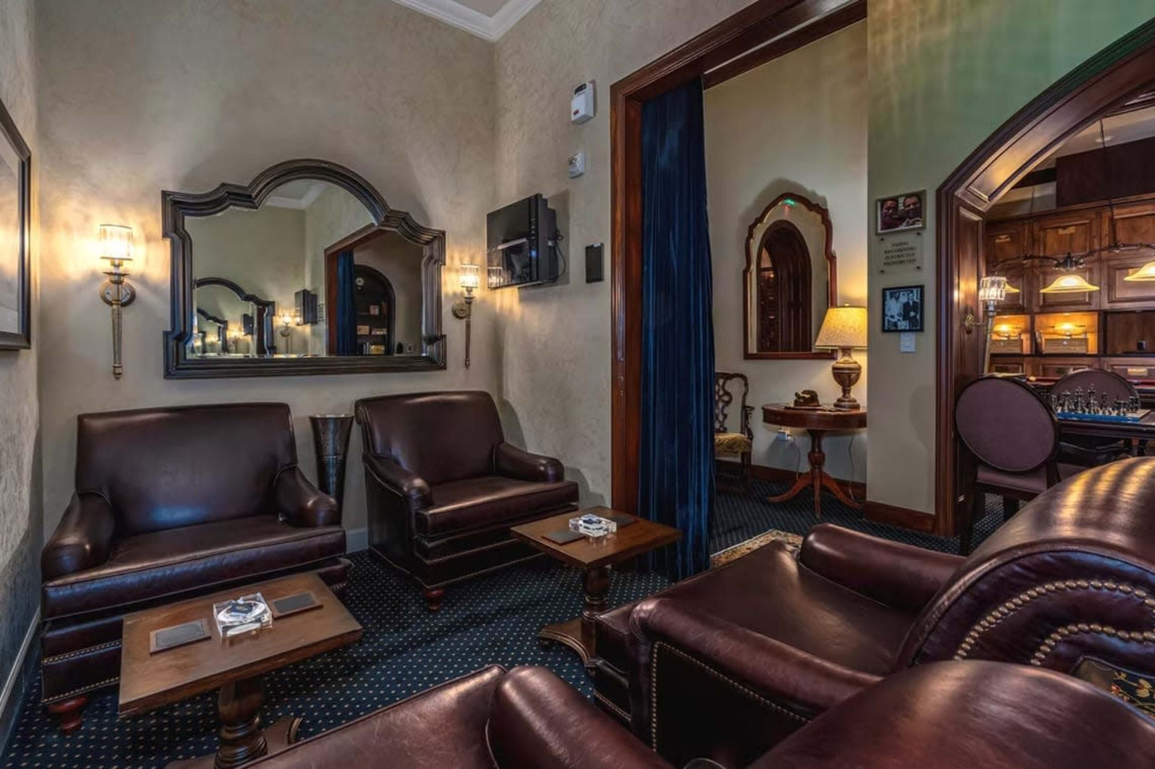 The image shows a cozy lounge area with brown leather seating, a large mirror on the wall, and an adjacent room visible through an archway.