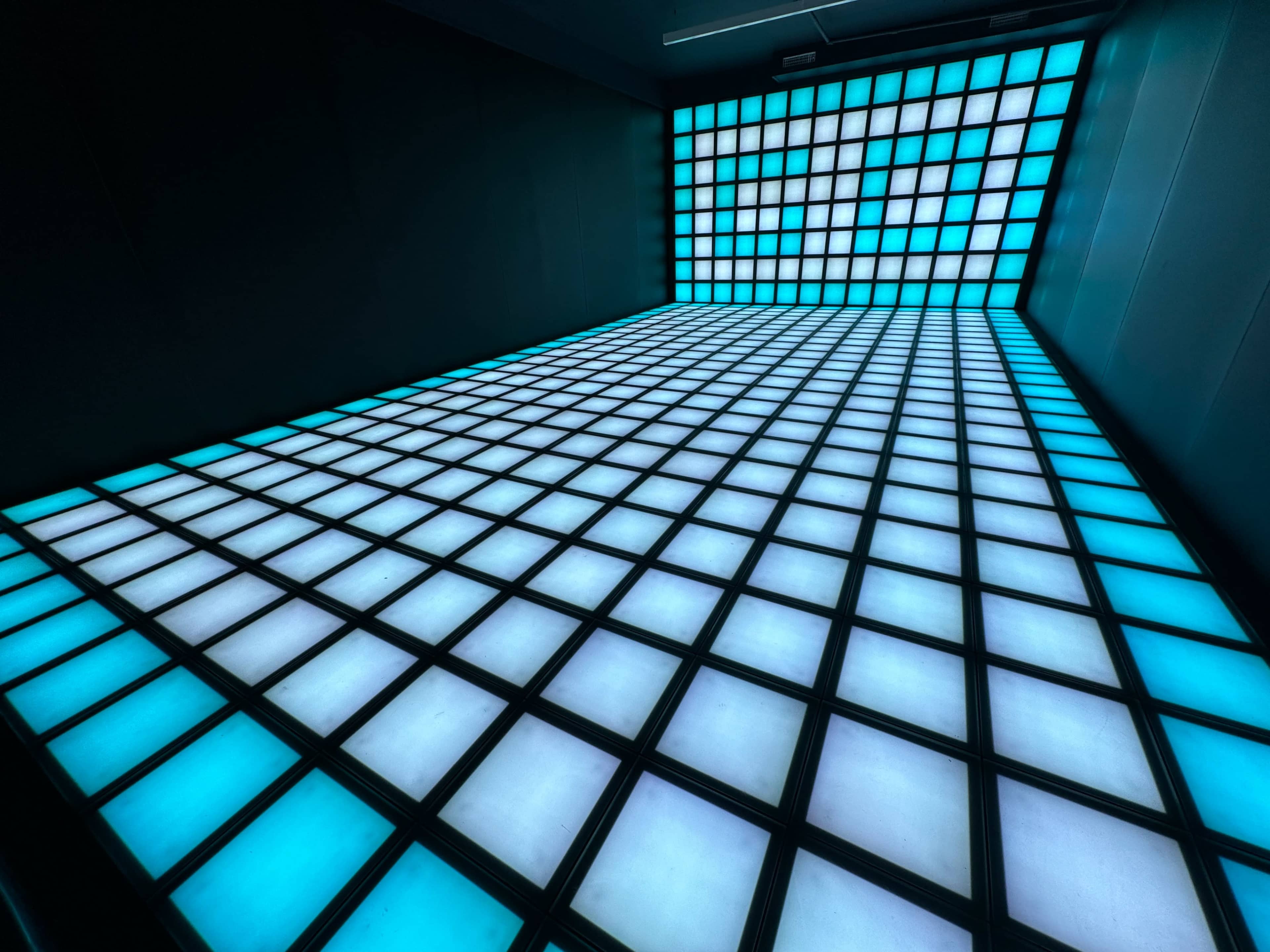 A room with walls and a floor covered in a grid of illuminated blue and white panels.