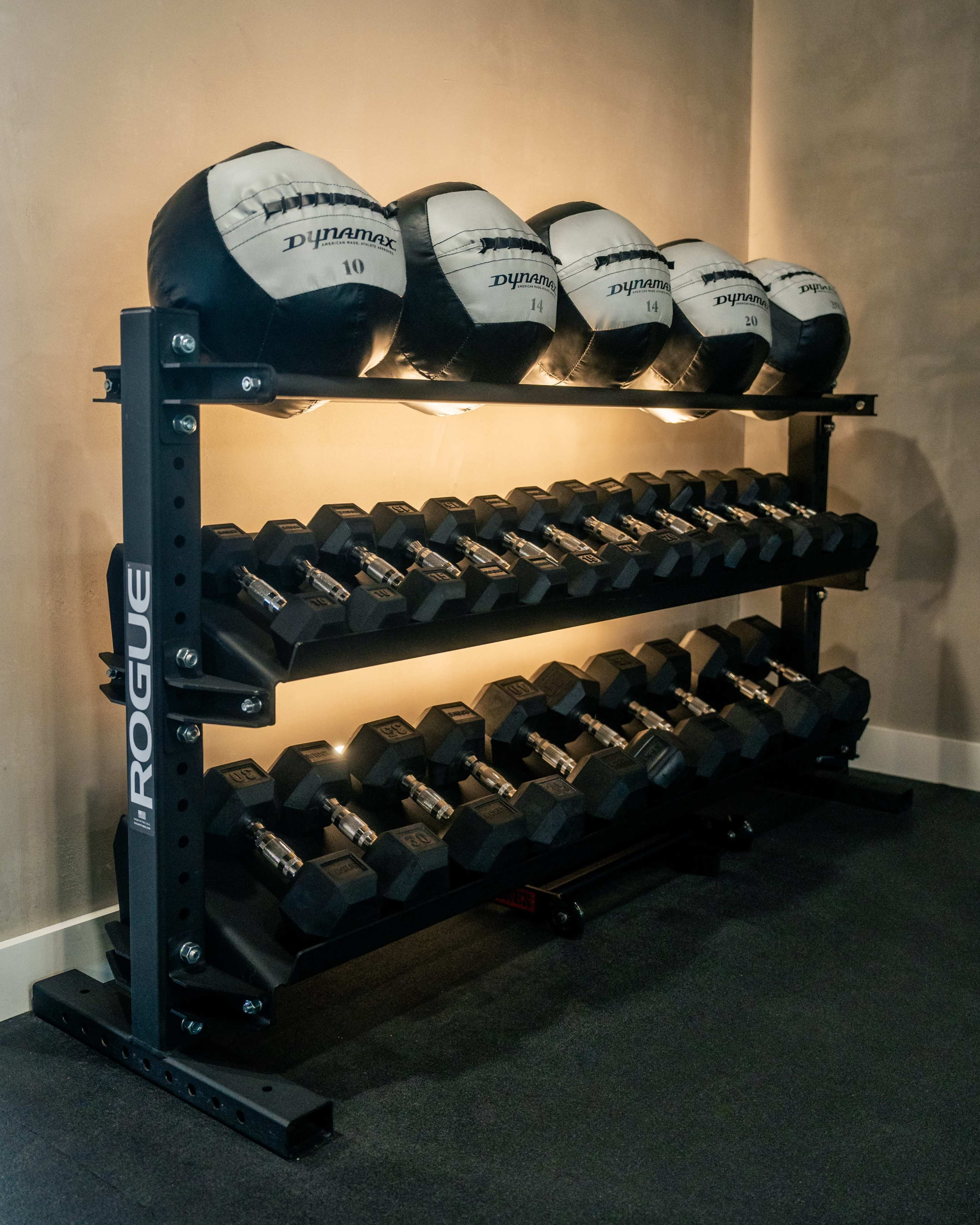 A rack displays a set of weights and medicine balls against a neutral wall.