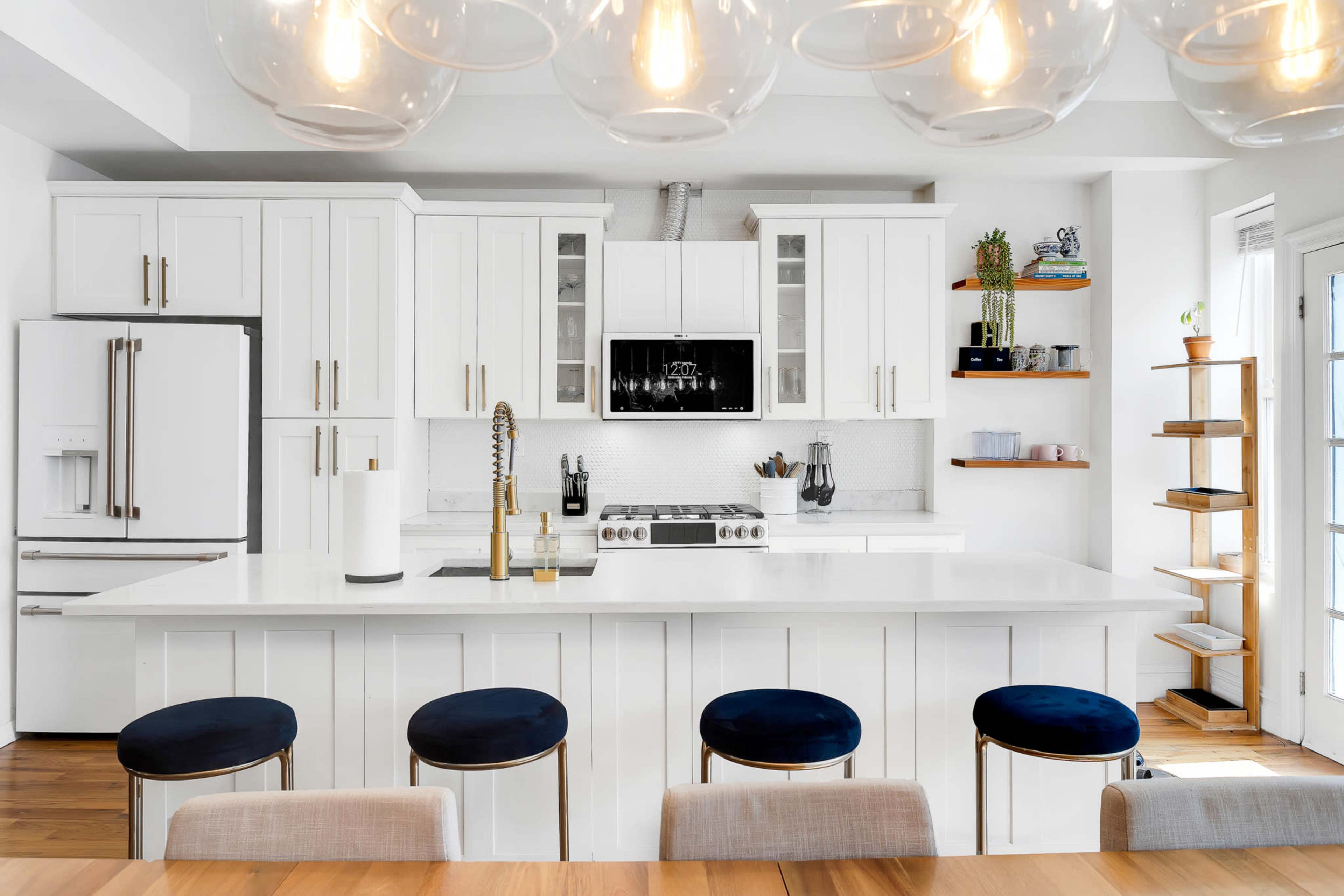 A modern kitchen with white cabinetry, a large island with bar stools, and a wall-mounted television.