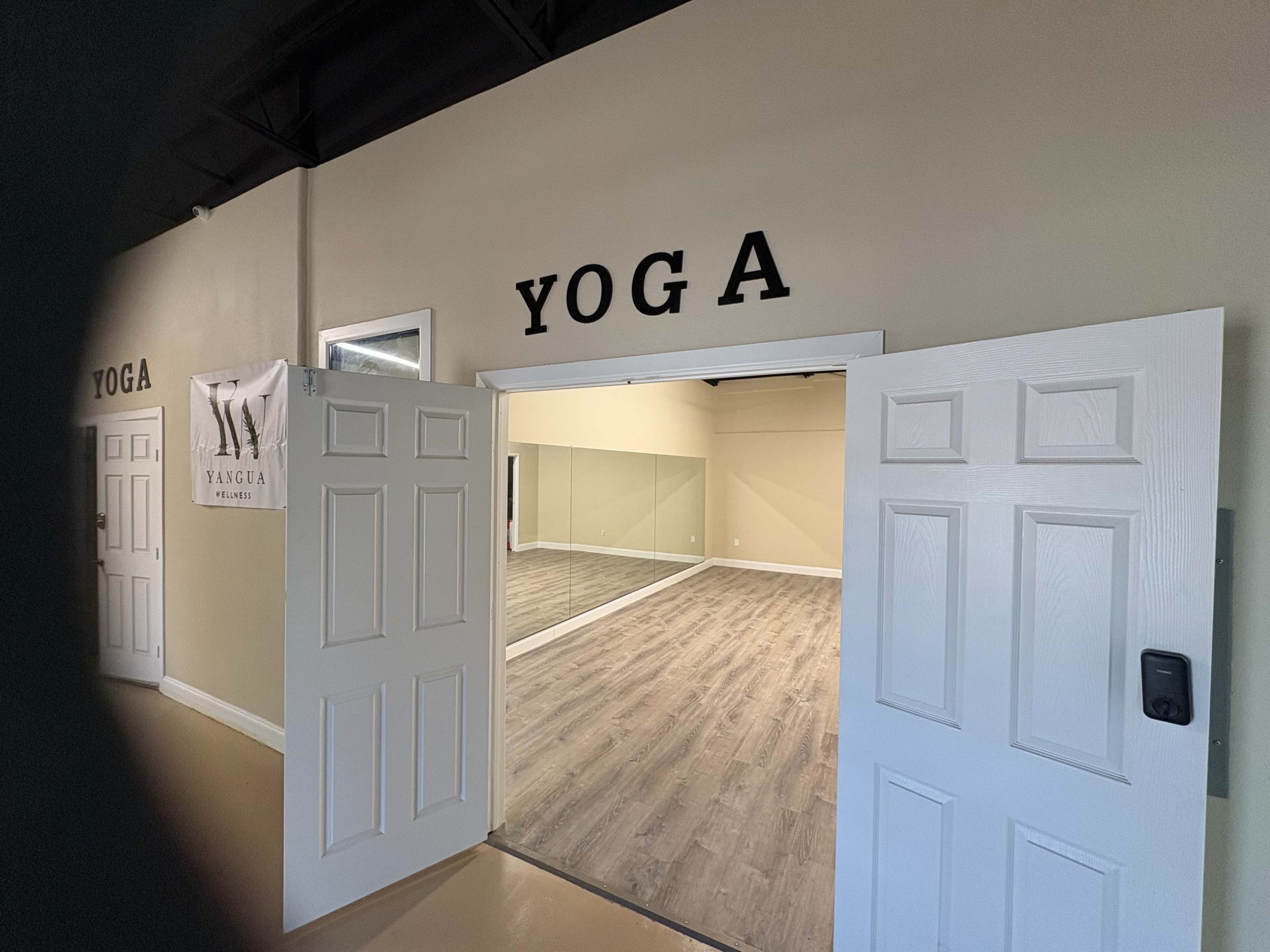 A spacious yoga studio with mirrored walls and wooden flooring is visible through open double doors.