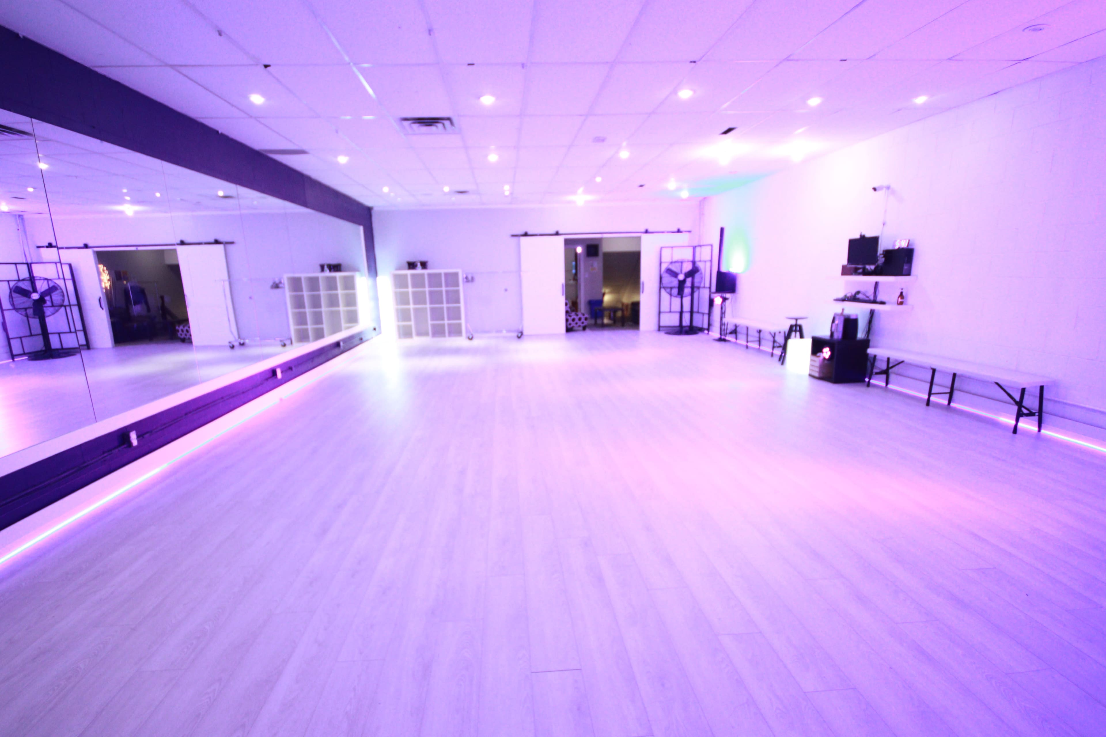 A spacious dance studio with purple lighting, large mirrors, and wooden floors.