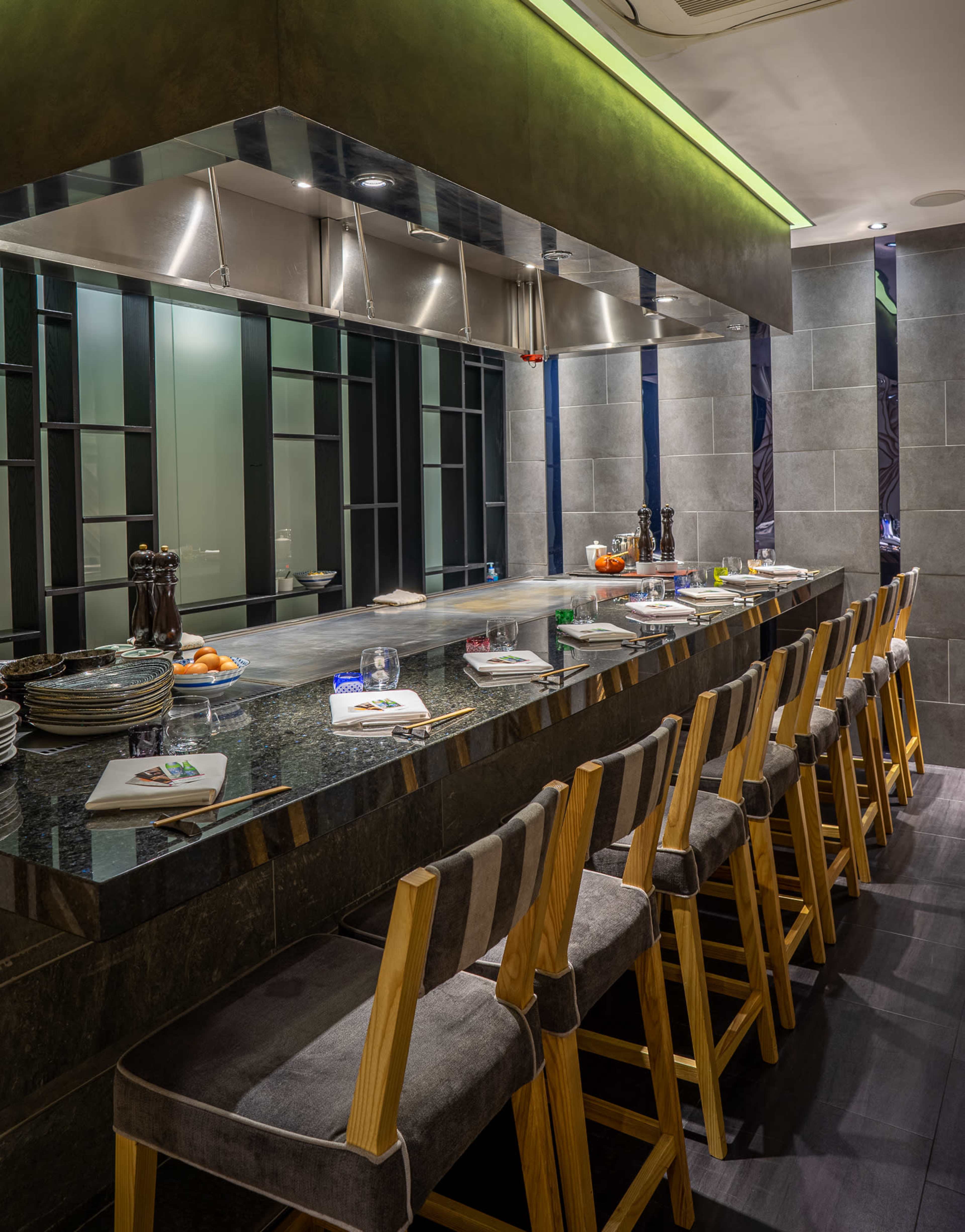 The image shows a modern dining counter with wooden stools and a sleek, tiled kitchen area in the background.