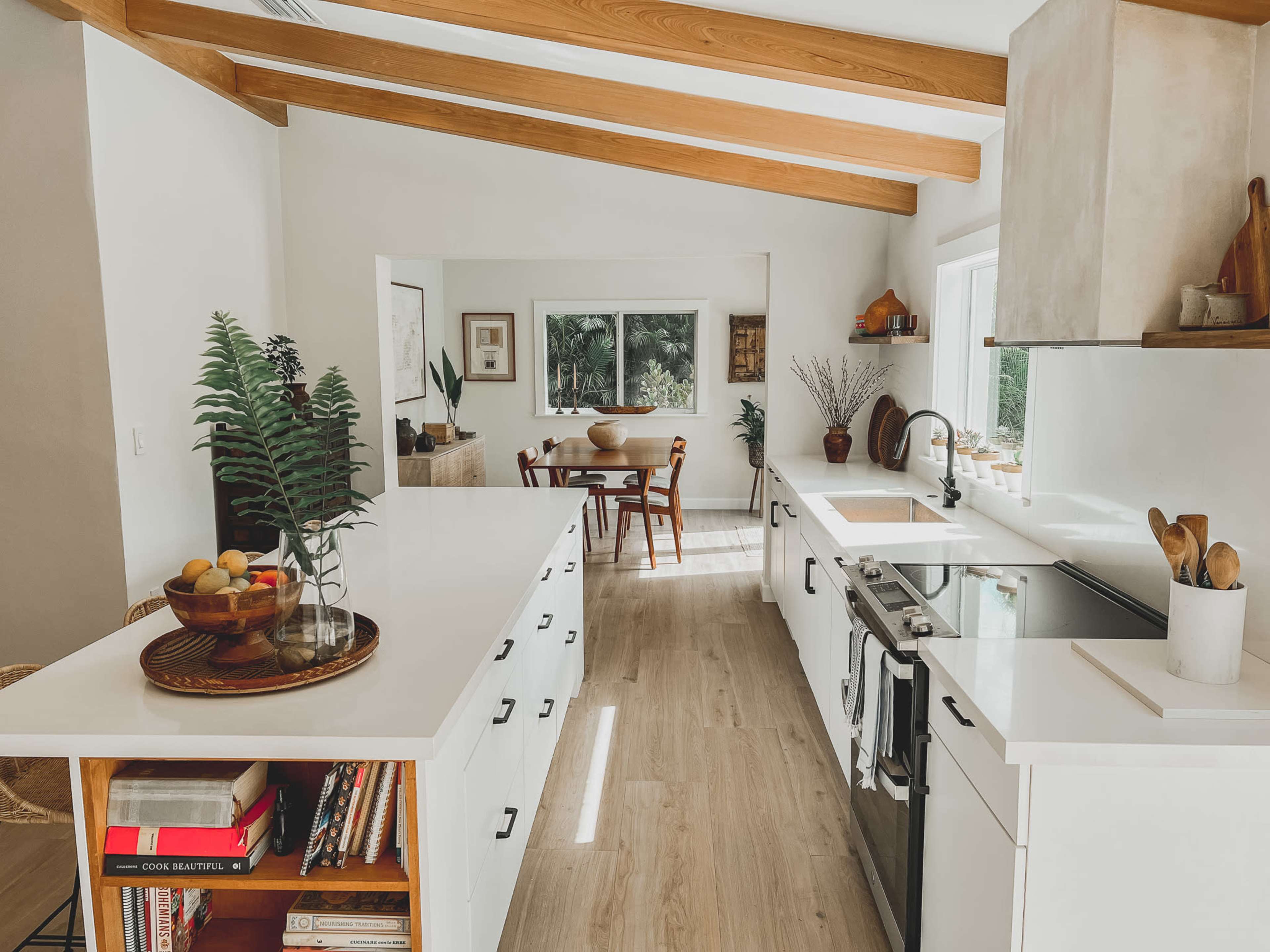 A modern kitchen features white cabinetry, wooden beams, and a central island with a fruit bowl.