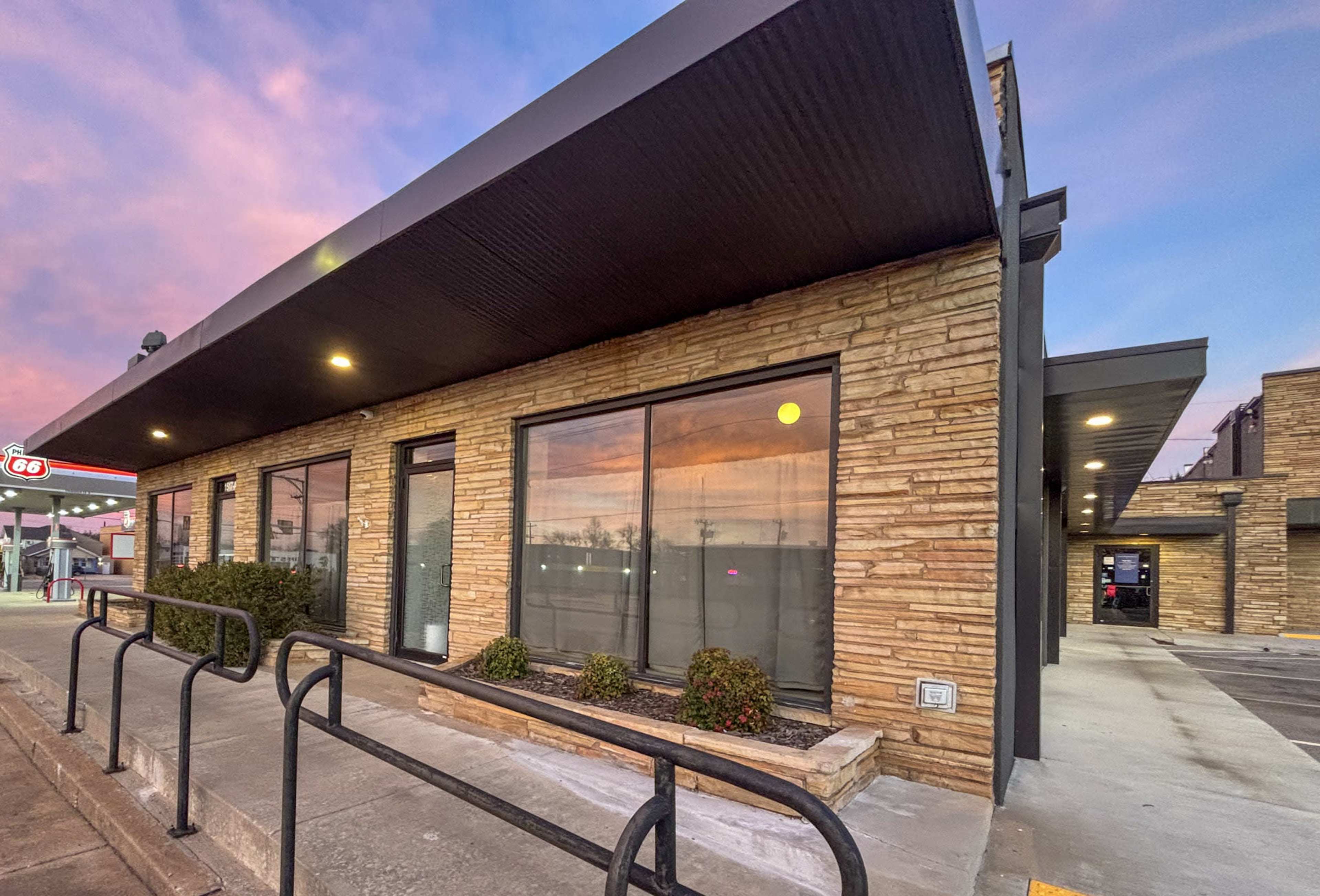 A modern commercial building with a stone facade and large windows is situated along a sidewalk, featuring a ramp and metal railings for accessibility.