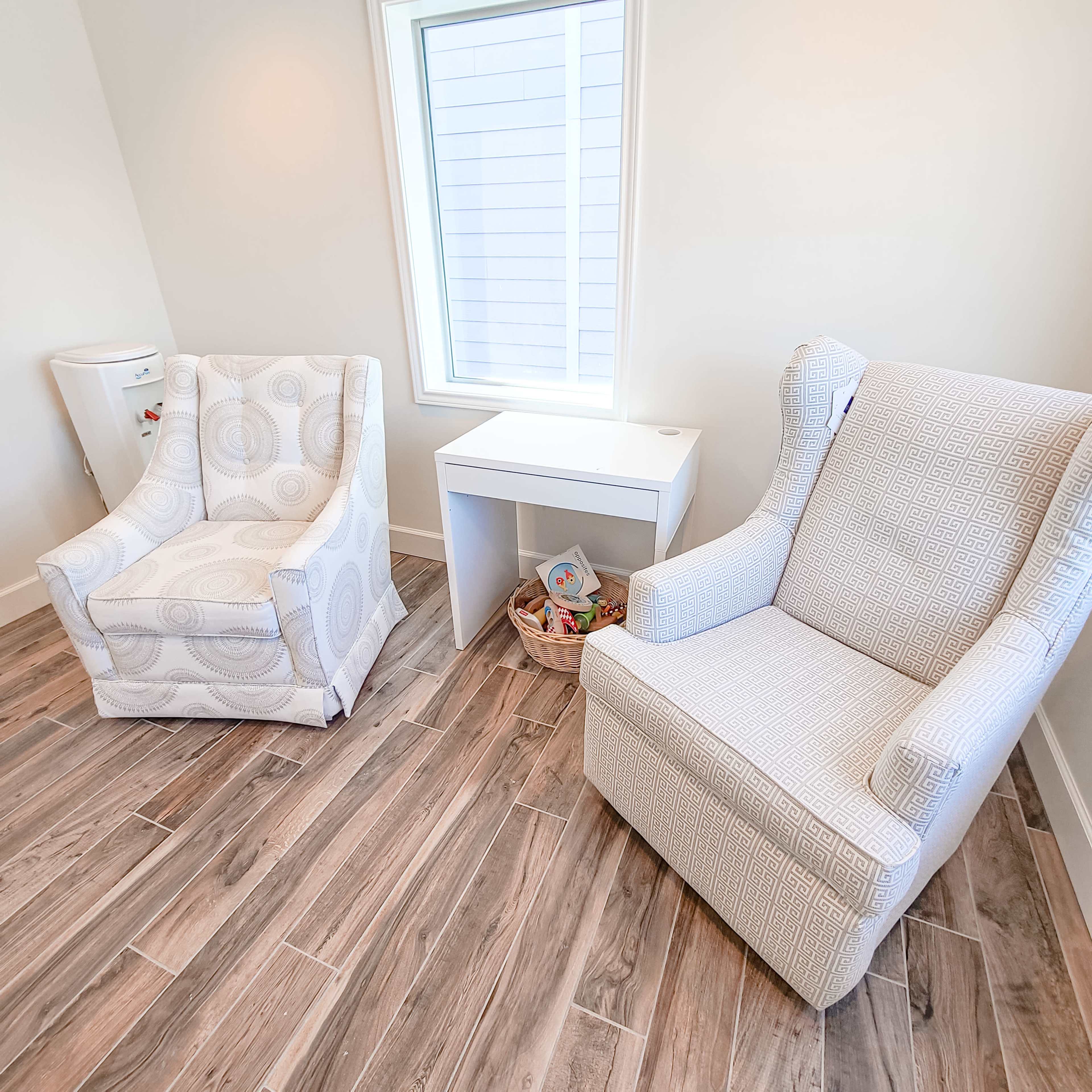Two patterned armchairs positioned beside a small white table in a brightly lit room with wood-like flooring.