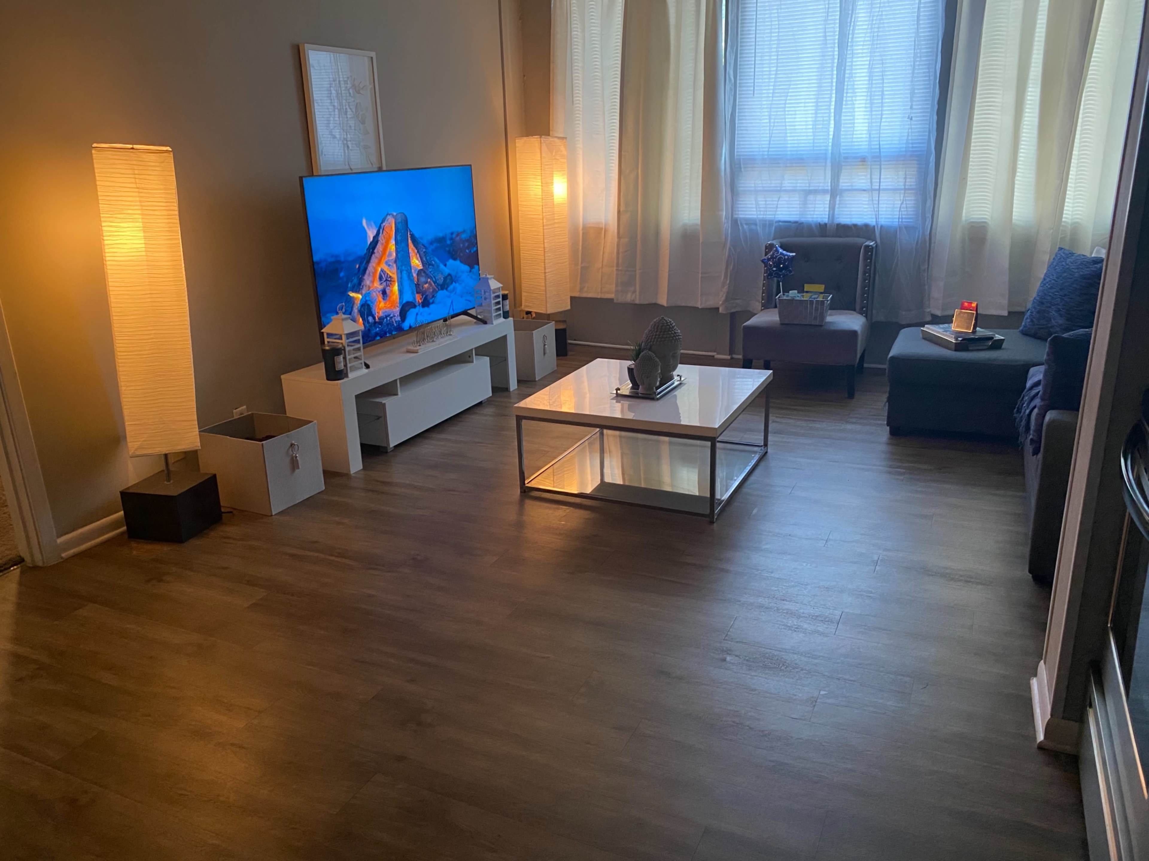 The image shows a living room with a large TV displaying a mountain scene, a coffee table, a sofa, and two floor lamps illuminating the space.