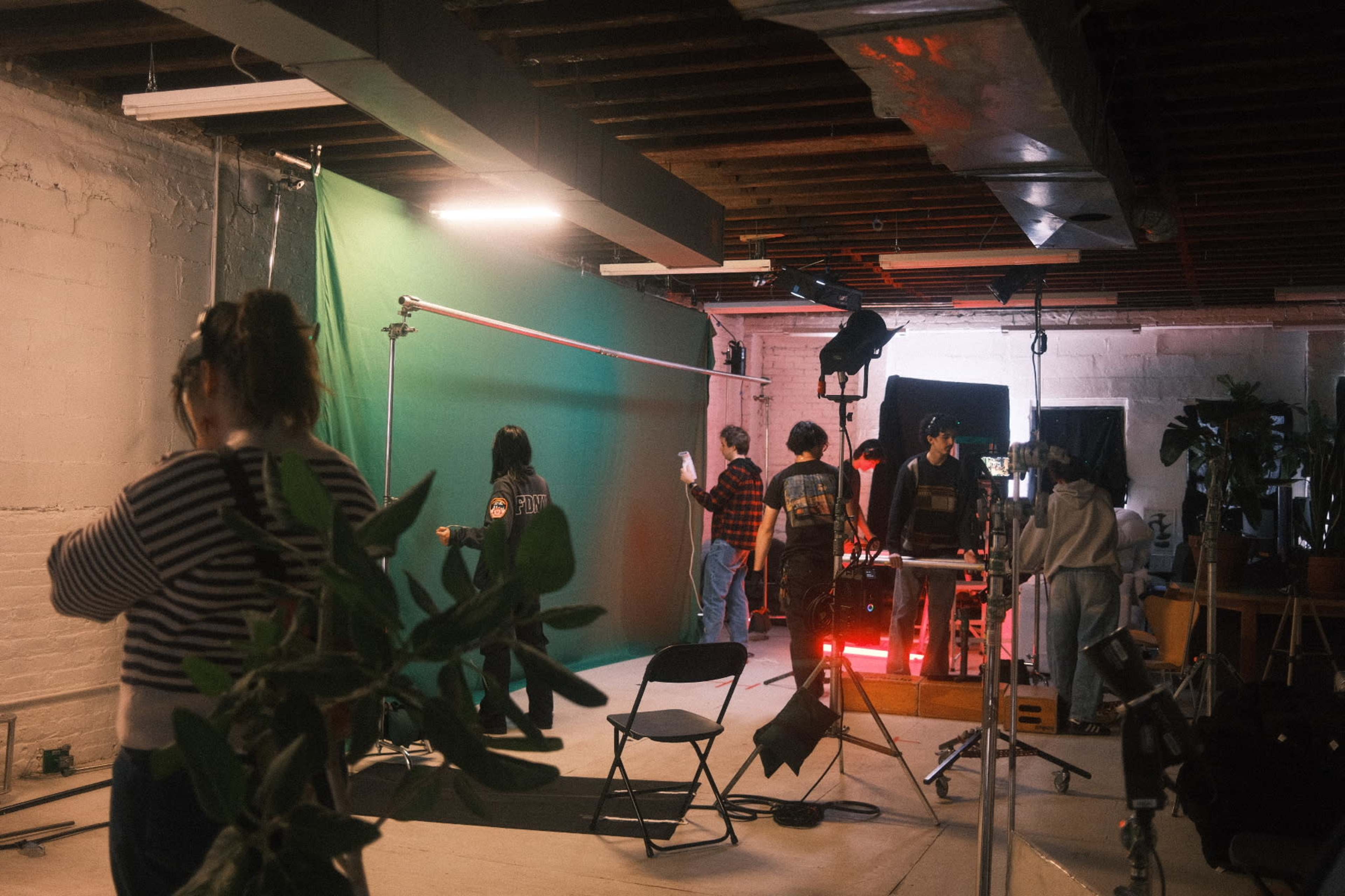 A group of people works in a studio setting with a green screen and various lighting equipment.