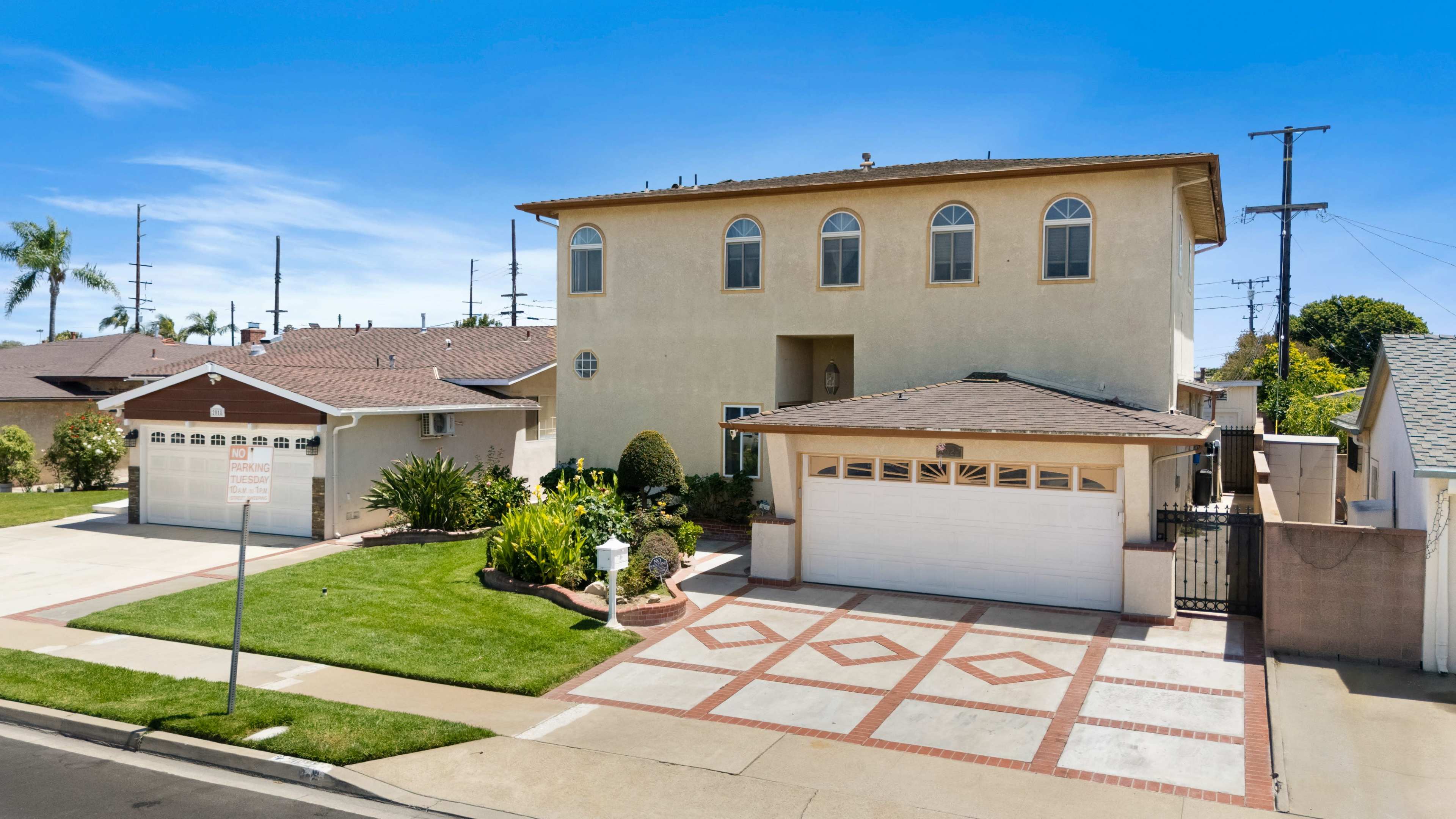 The image shows a large two-story house with a landscaped front yard and a brick-patterned driveway.