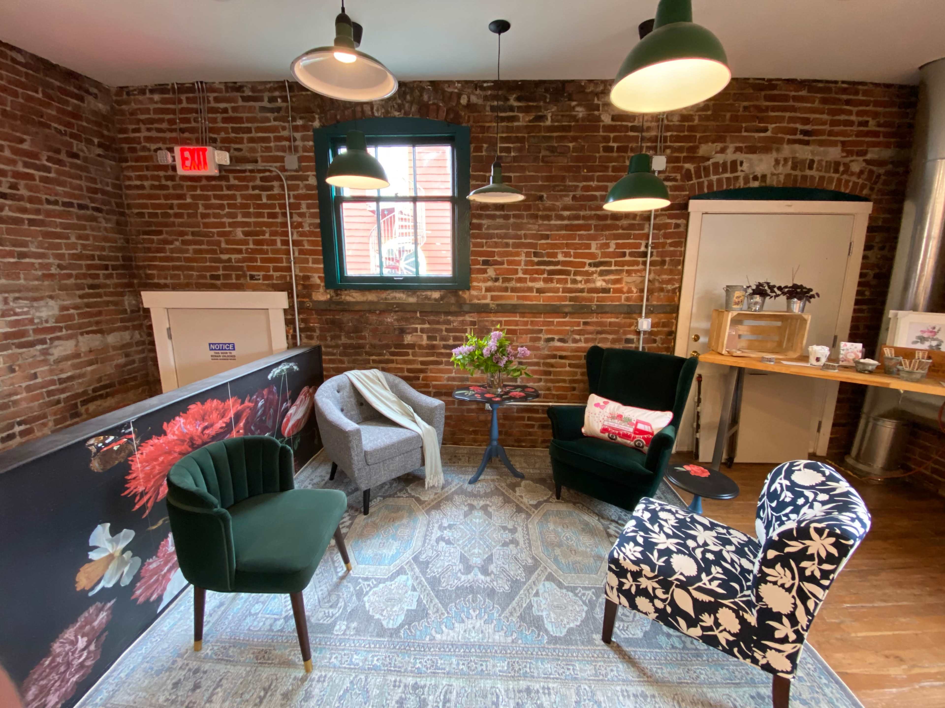 A cozy seating area with a mix of chairs on a patterned rug, surrounded by exposed brick walls and lit by pendant lights.