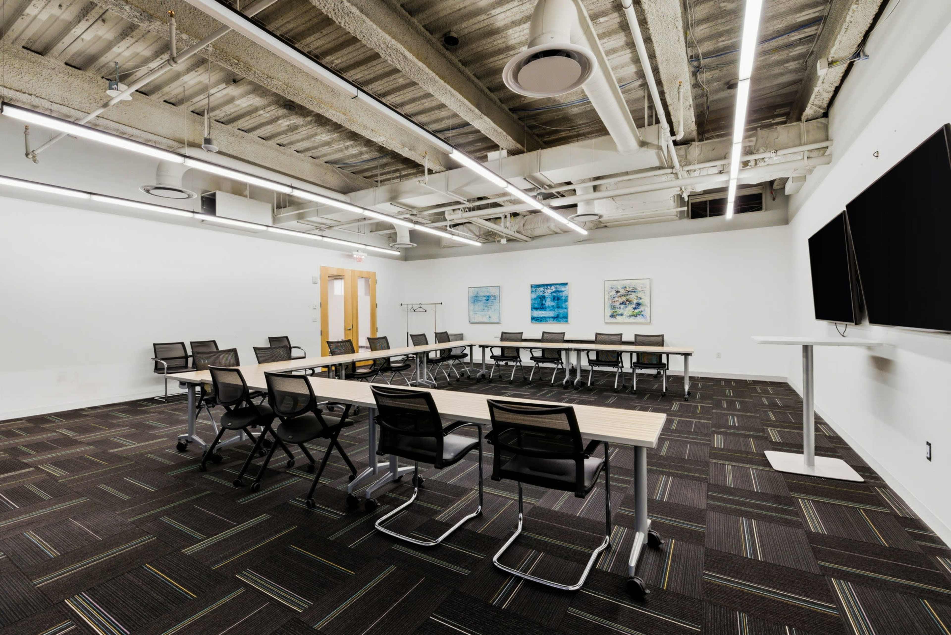 The image shows a modern conference room with a long table, several chairs, and a large screen on the wall.