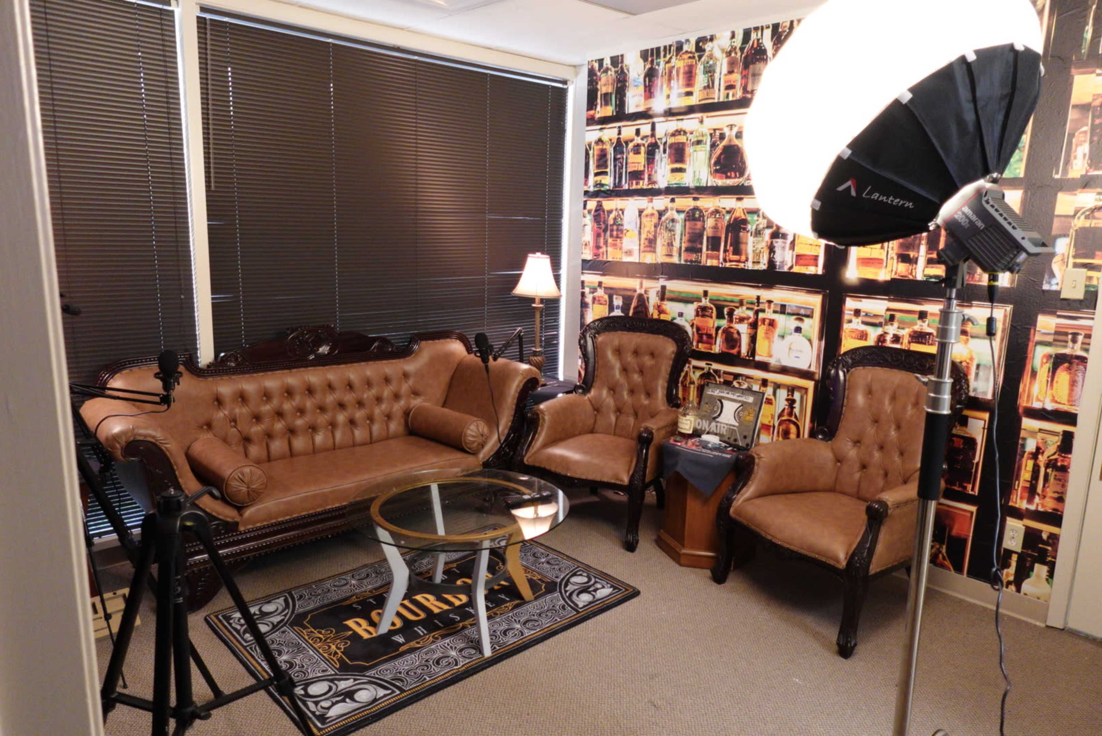 A small sitting area with tufted leather sofas, a glass coffee table, and a backdrop of a patterned wallpaper featuring bottles.