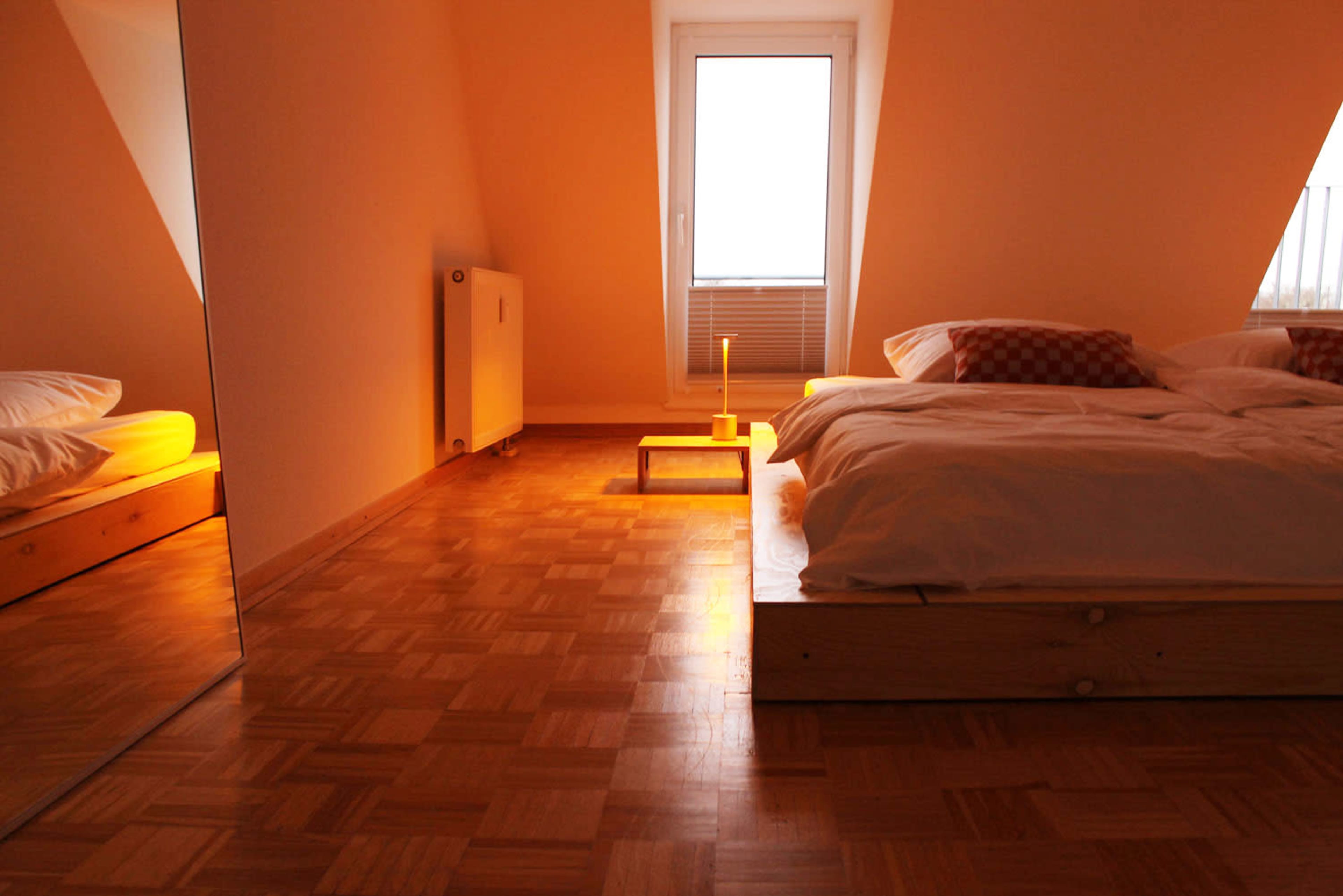 A softly lit bedroom features a wooden bed with white bedding and a small table holding a candle.