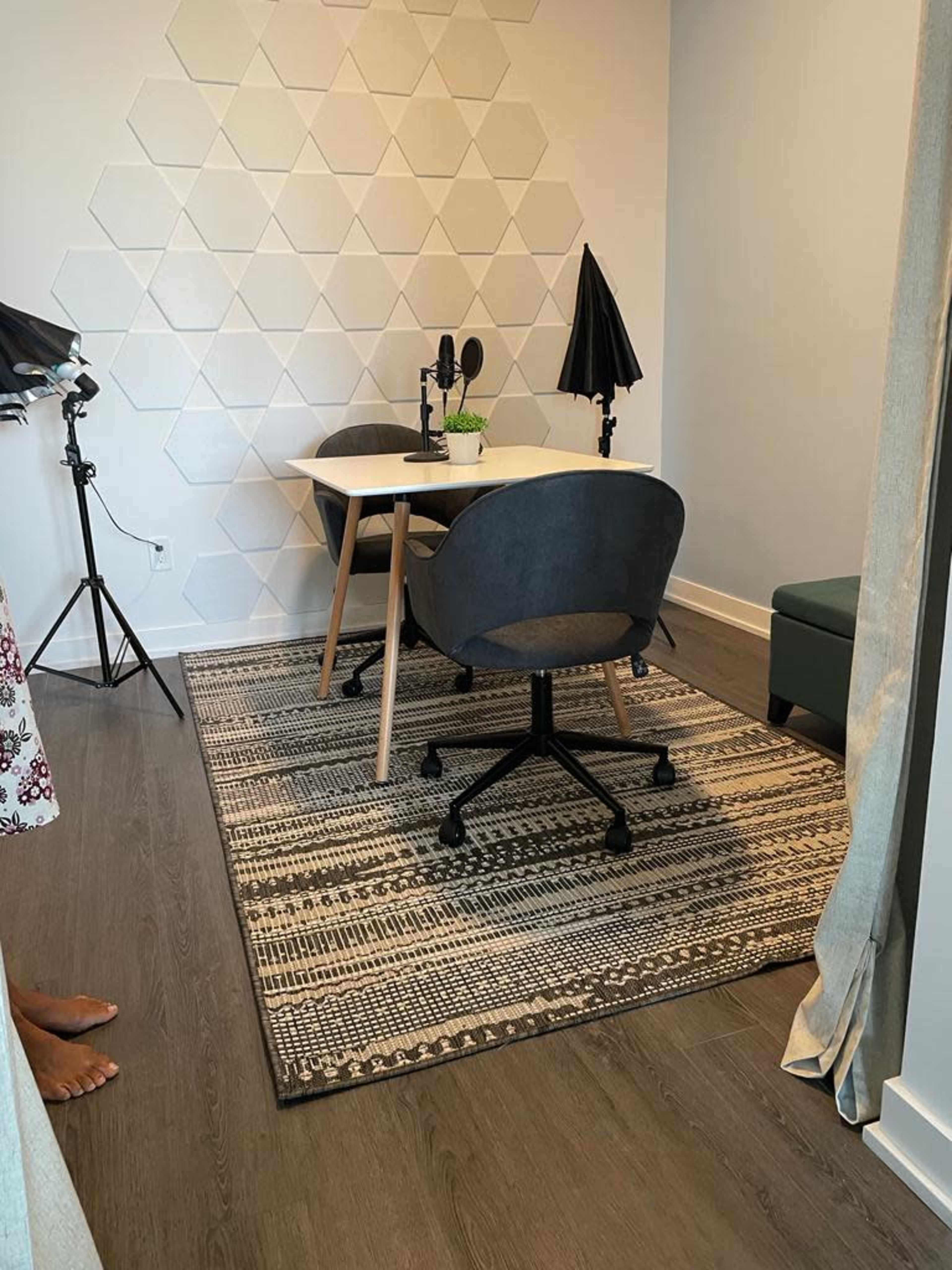 A small recording studio features a table with microphones, two chairs, and a patterned rug on the floor.