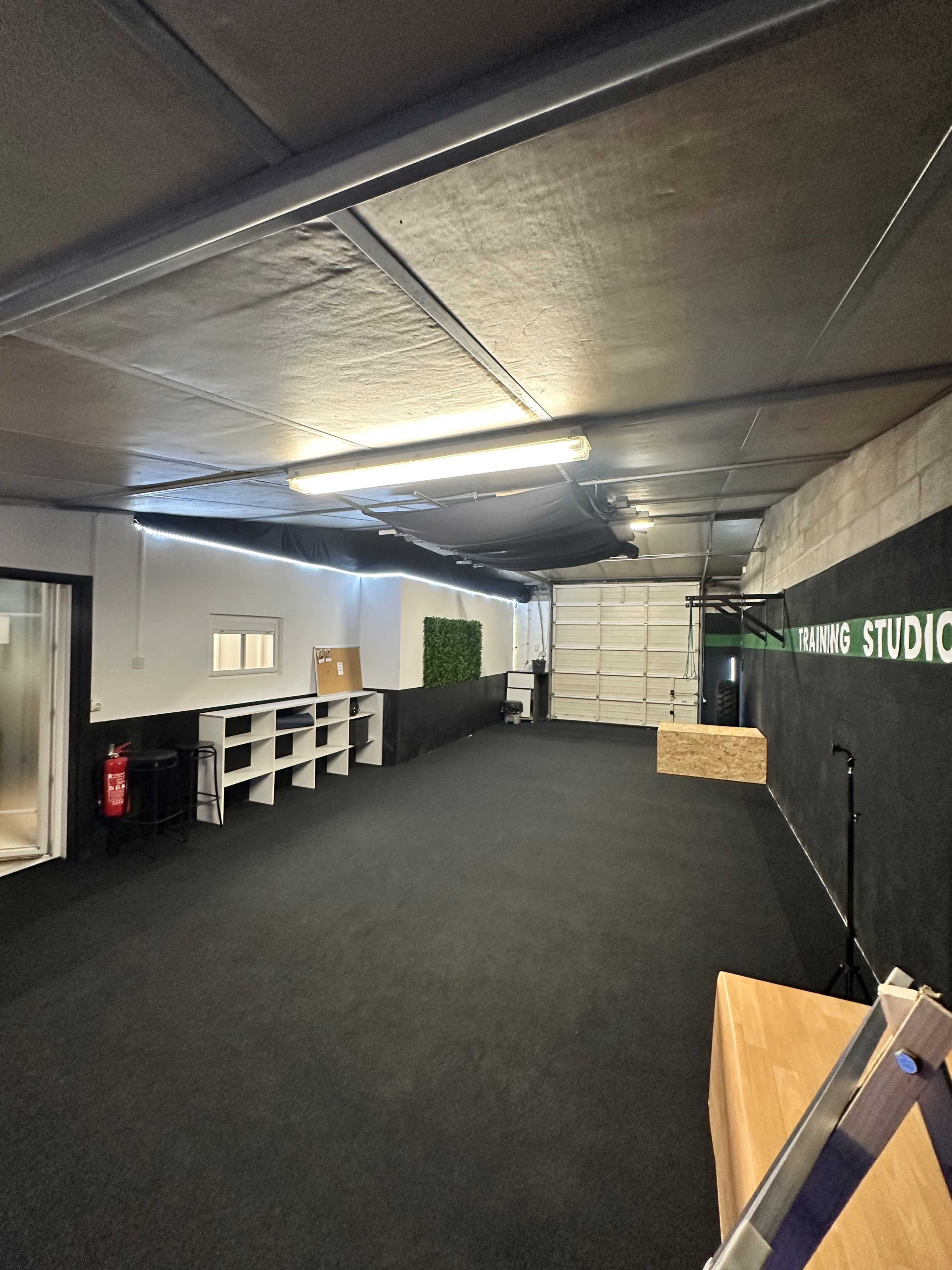 The image shows a spacious, well-lit training studio with black flooring, minimalist shelving, and a wall featuring the text "TRAINING STUDIO."