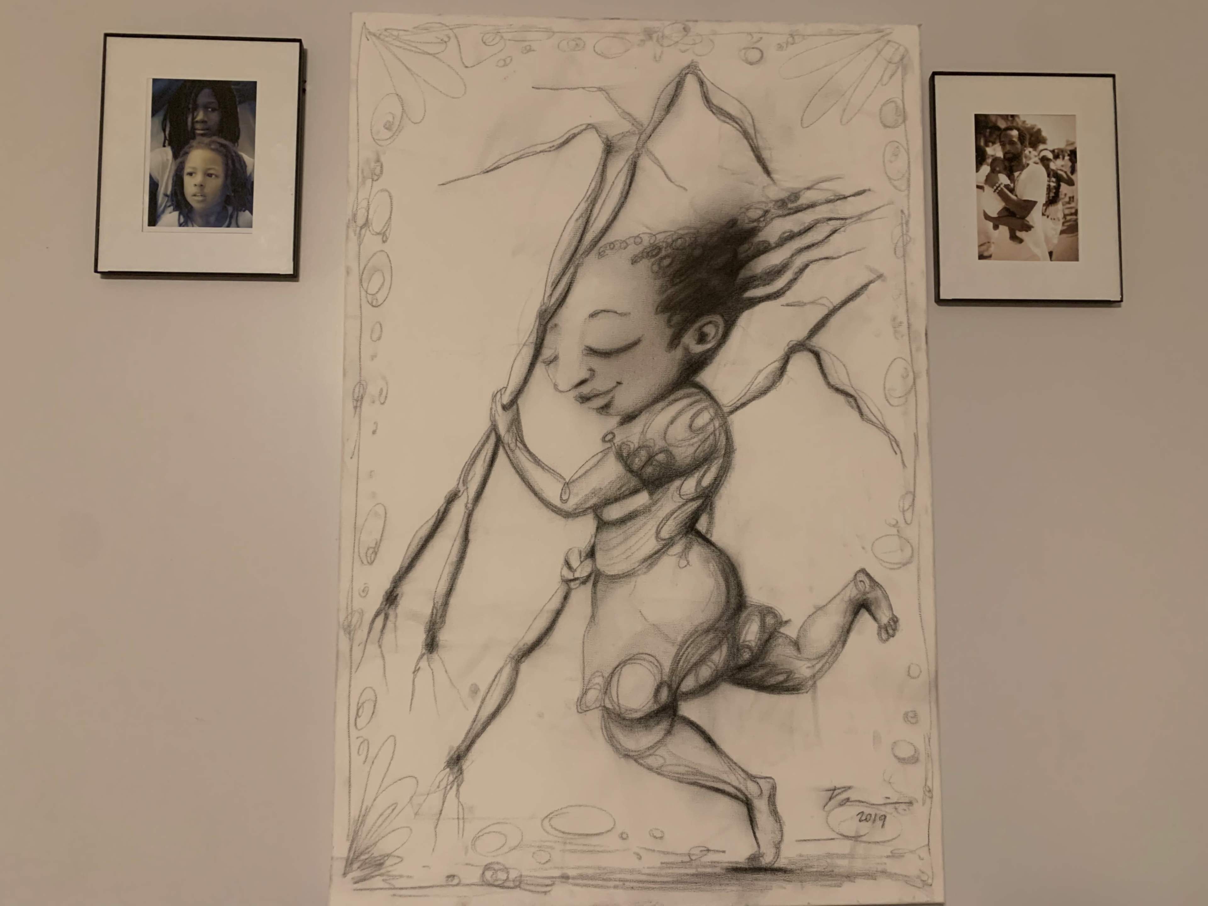 A large, stylized drawing of a figure running and embracing a rock formation, flanked by two smaller framed photographs on the wall.