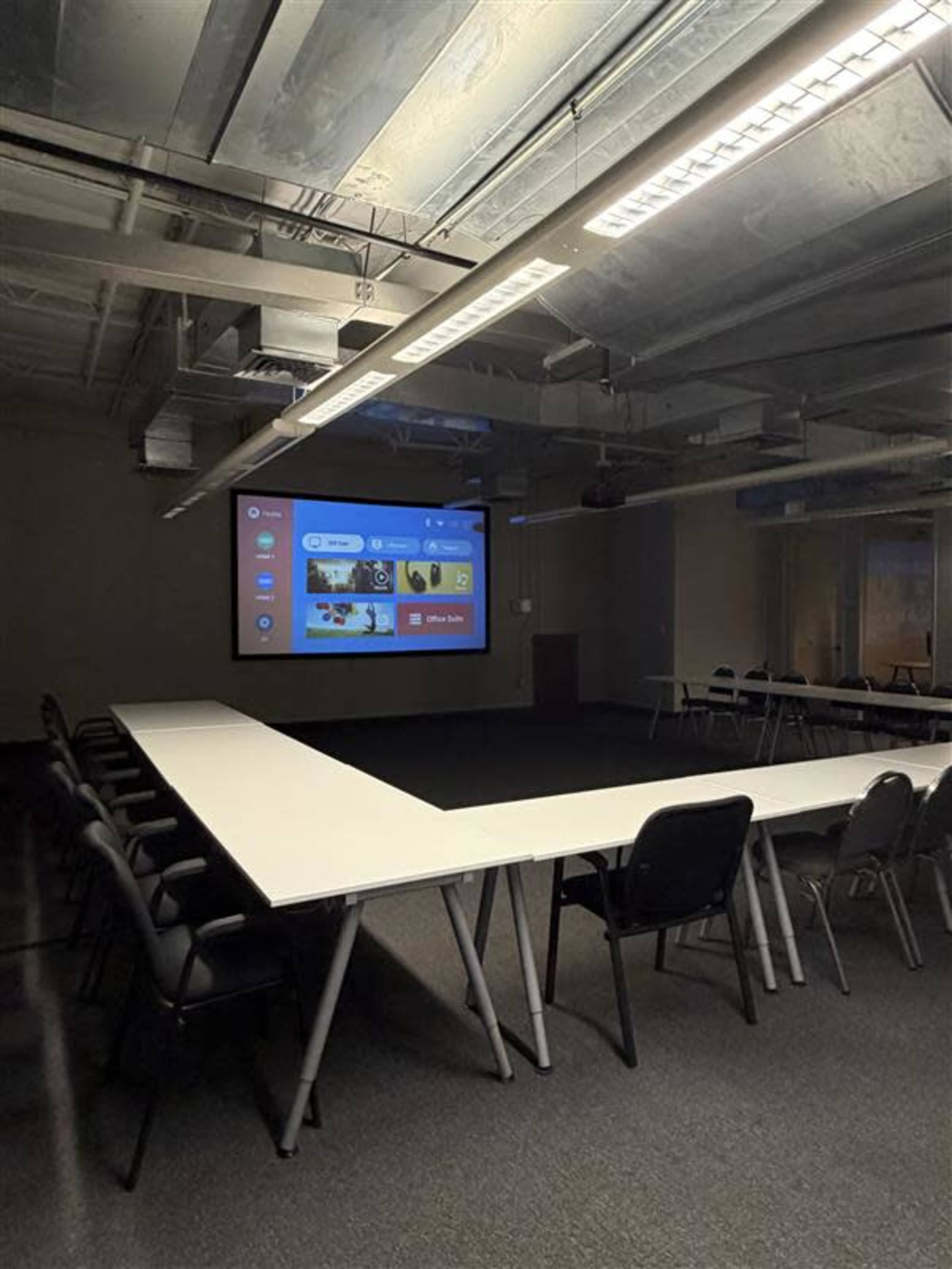 The image shows a modern conference room with a large screen displaying a menu and several tables arranged in a U-shape around the perimeter.