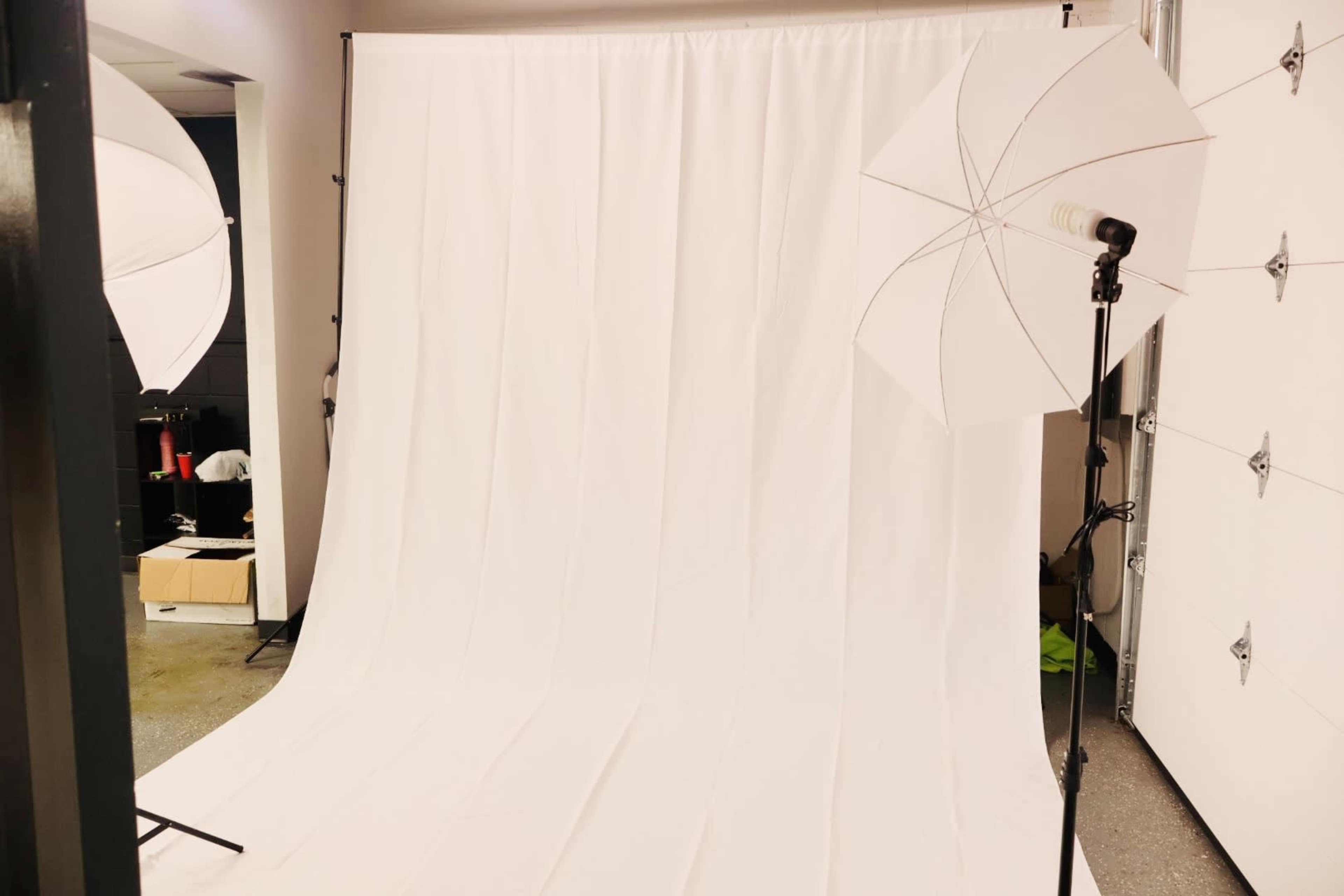 A photography studio setup with a white backdrop and two white umbrella lights positioned on either side.