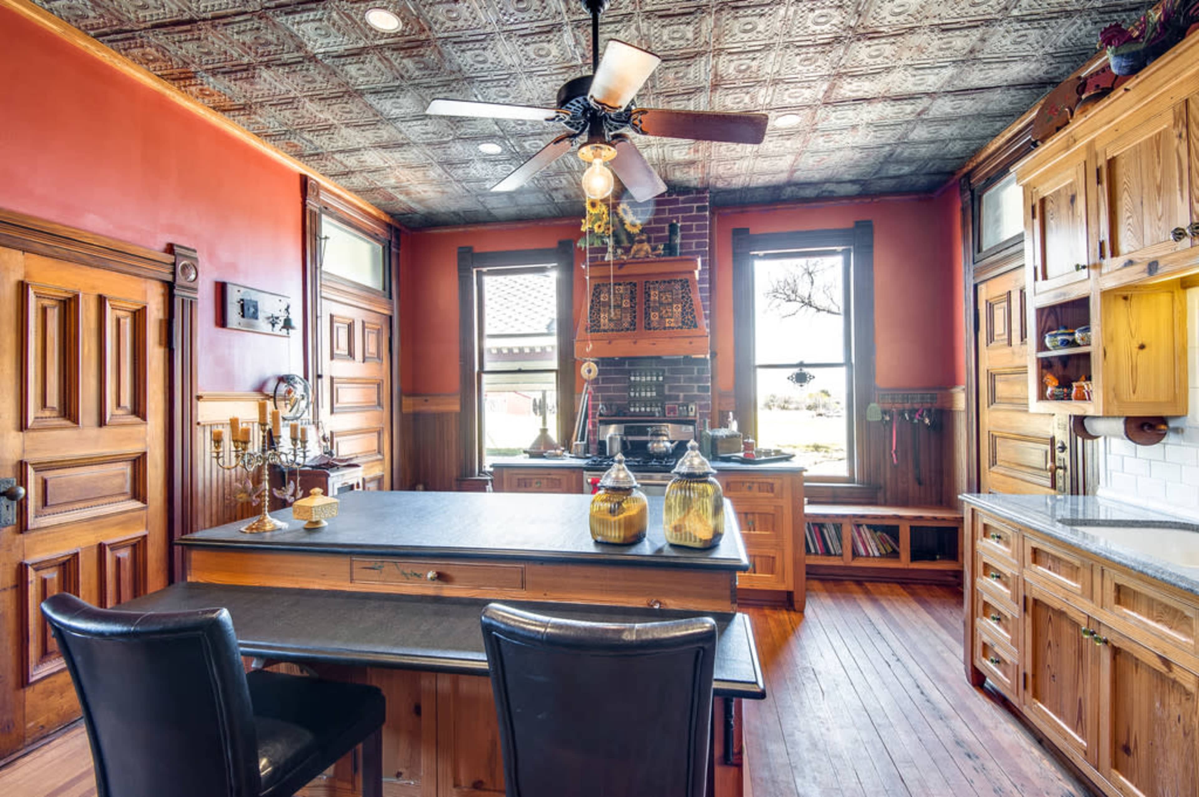 The kitchen features wooden cabinetry, a central island with a black countertop, and a ceiling adorned with decorative tin tiles.