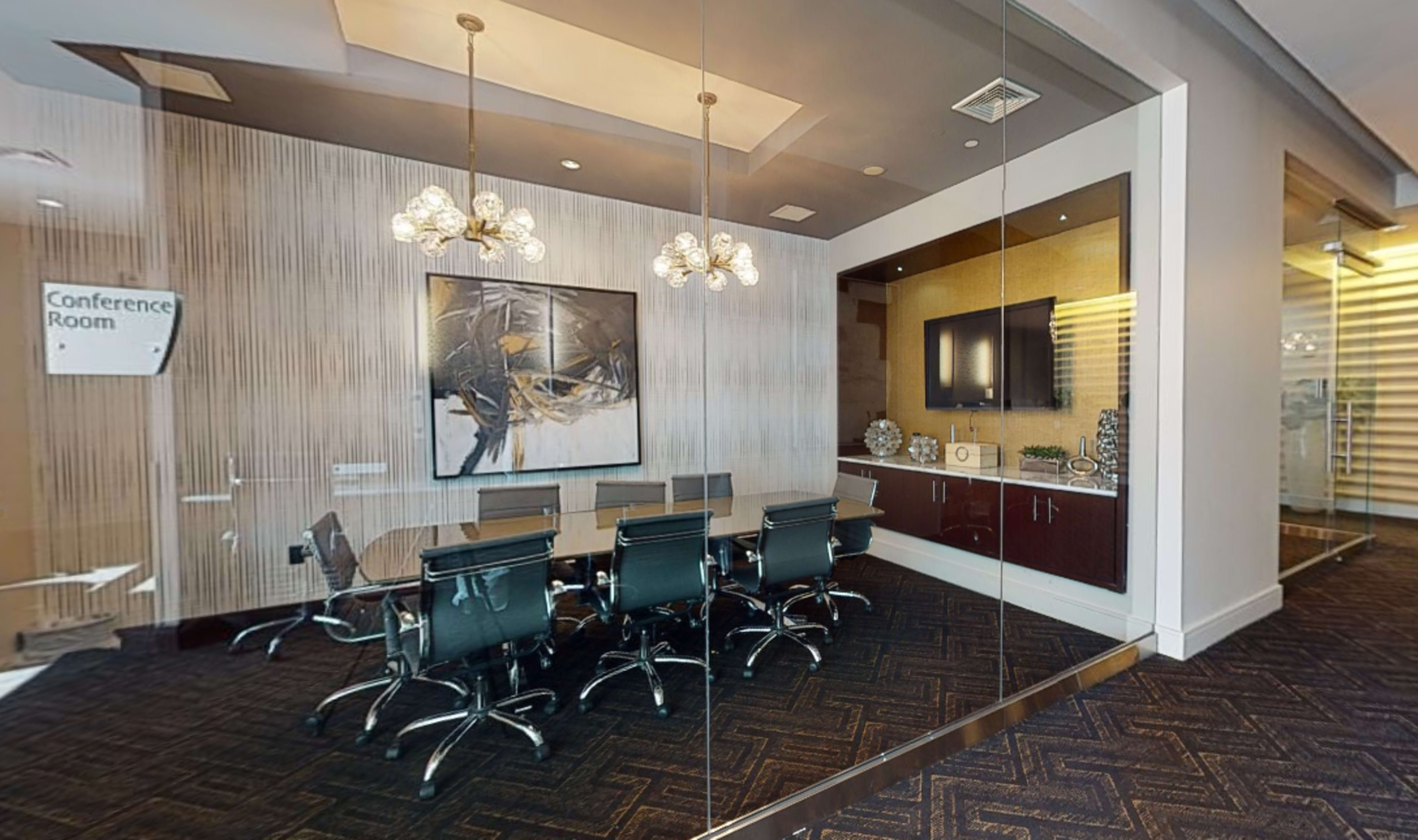 The image shows a modern conference room with a large table, black chairs, and a decorative wall featuring a television and artwork.