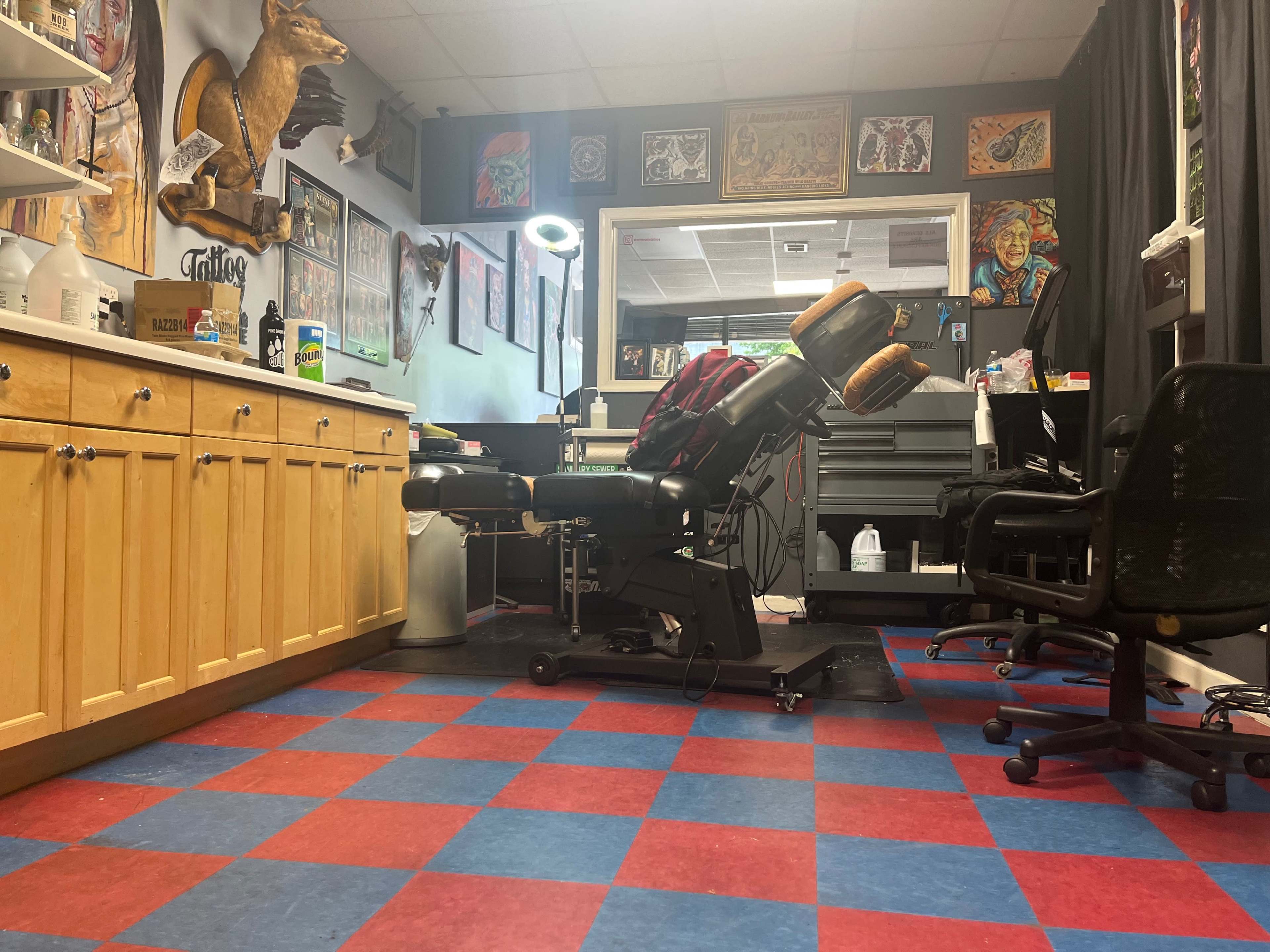 A tattoo parlor with a tattoo chair, workstations, and colorful checkered flooring.
