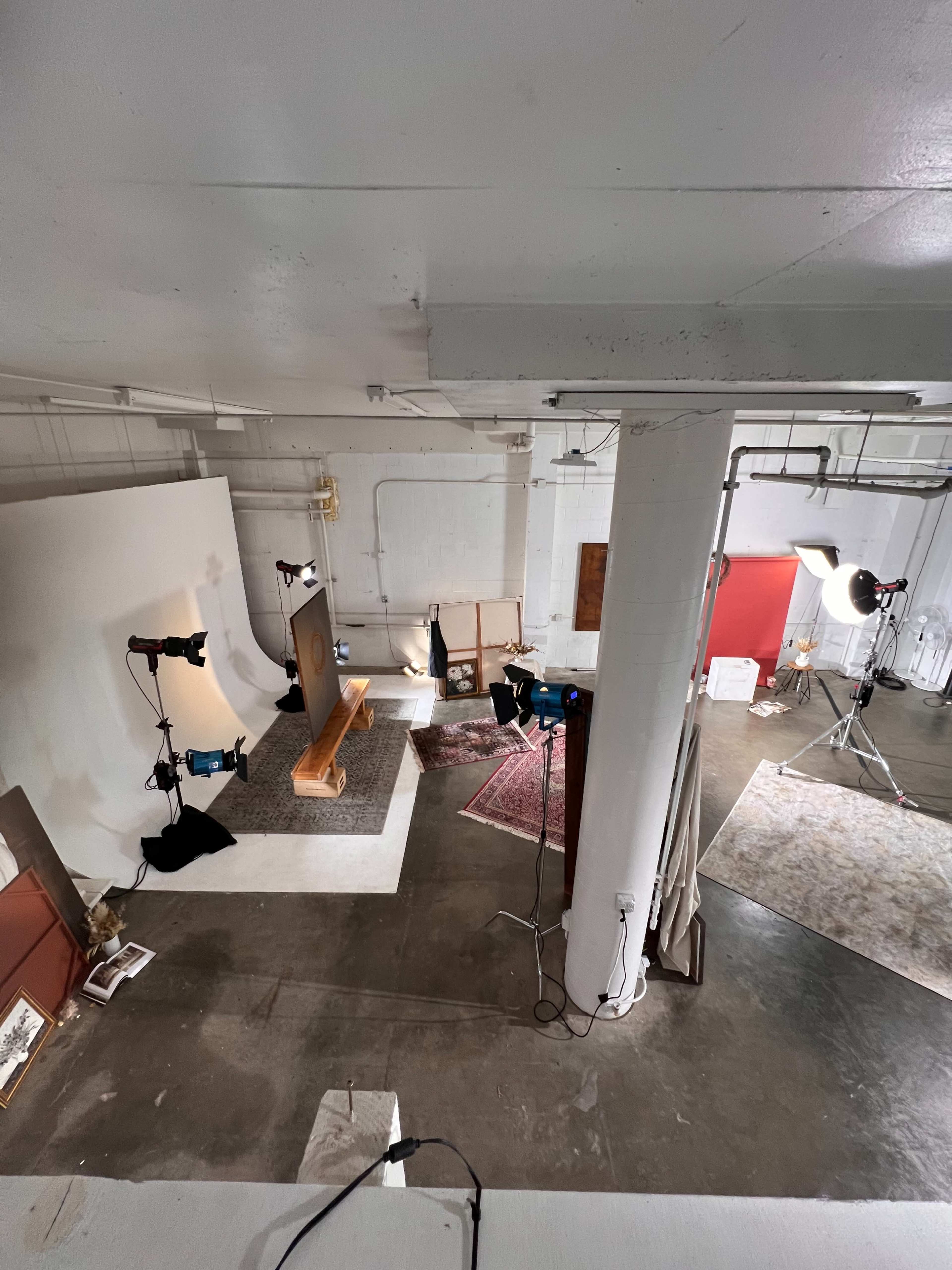 The image shows a well-lit studio space with a large backdrop, multiple cameras, and tripods set up for a photo or video shoot.