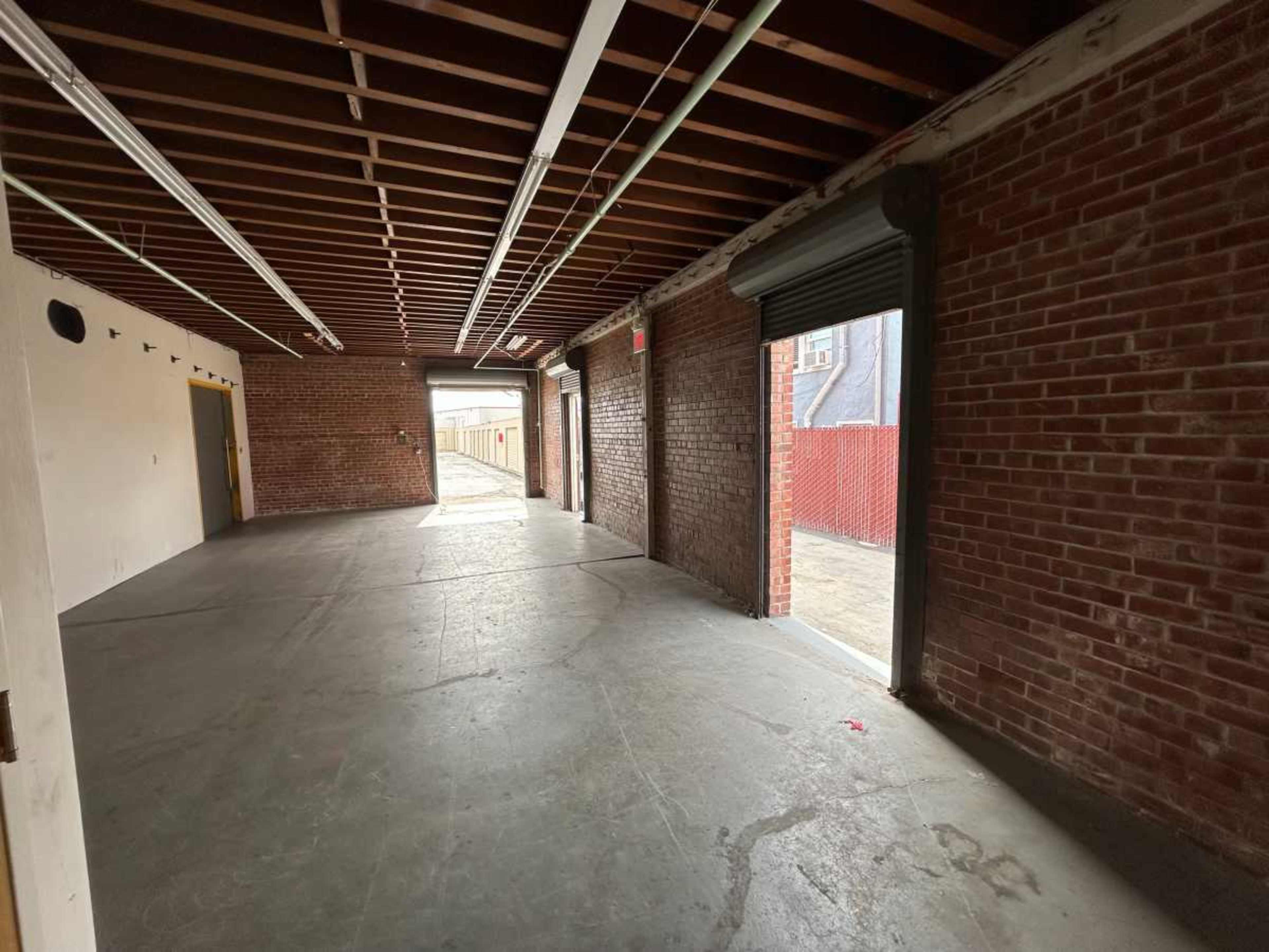 An empty, industrial-style room with exposed brick walls and a concrete floor, featuring roll-up doors at either end.