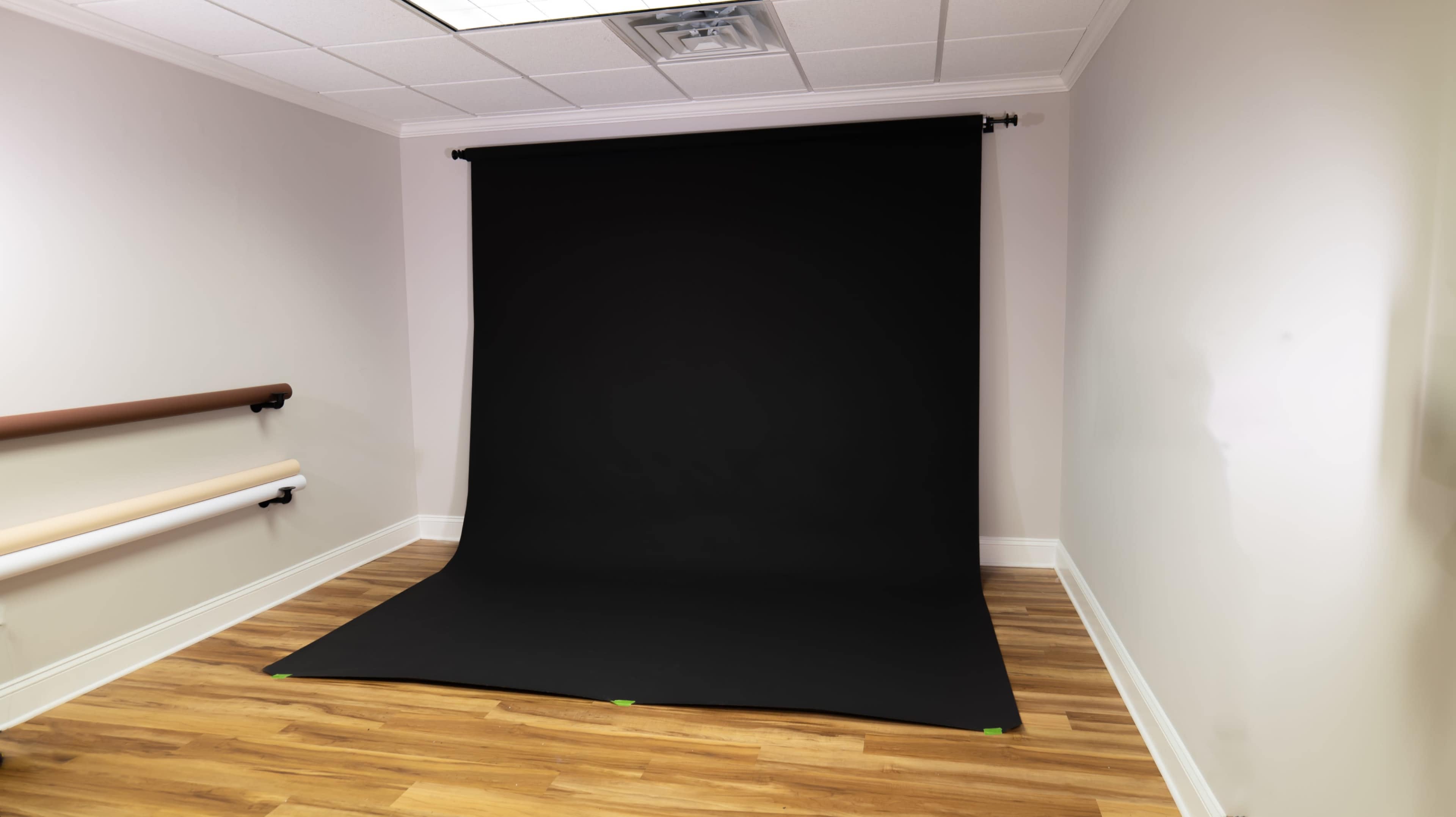The image shows a photography studio with a black backdrop set up against a plain wall and wooden flooring.
