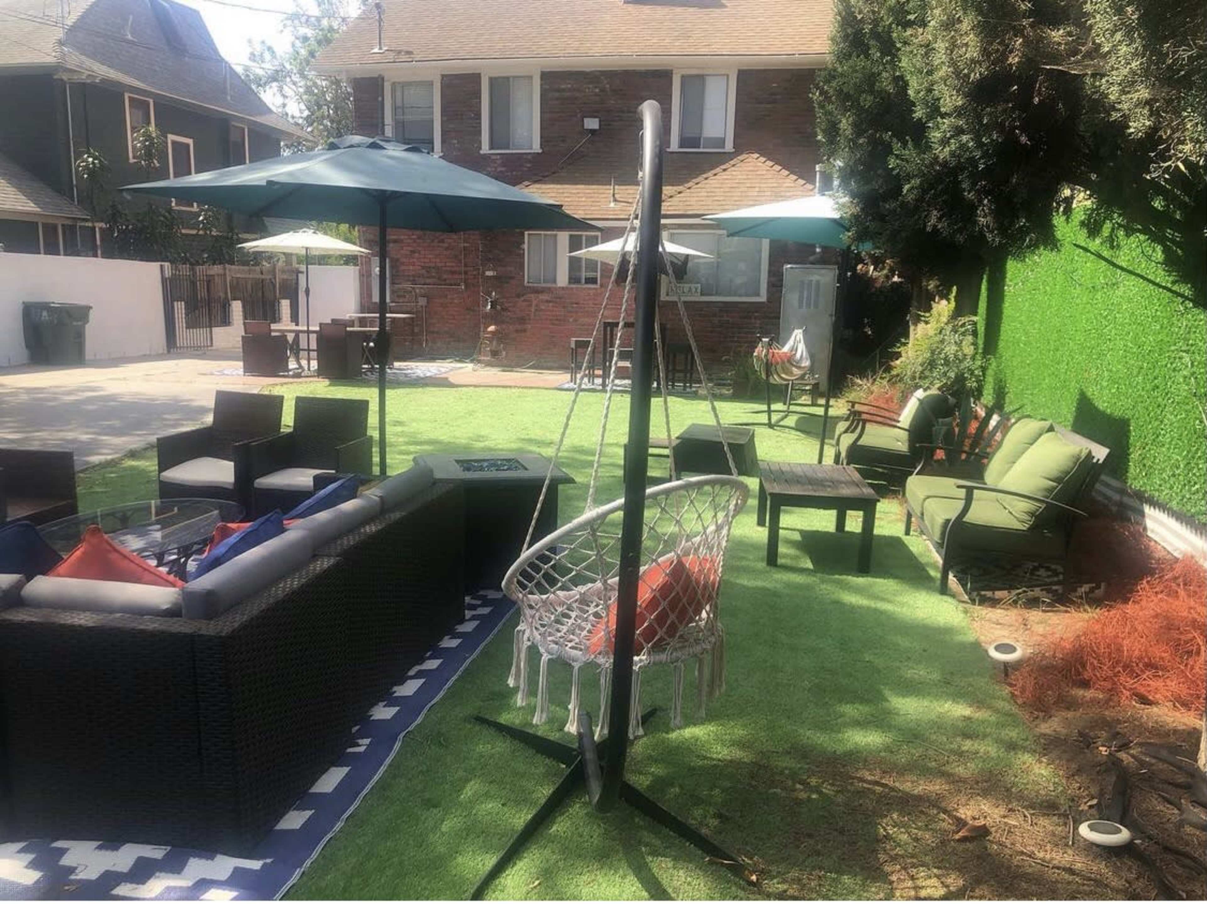 A backyard with seating areas, a hanging swing, umbrellas, and green artificial grass.