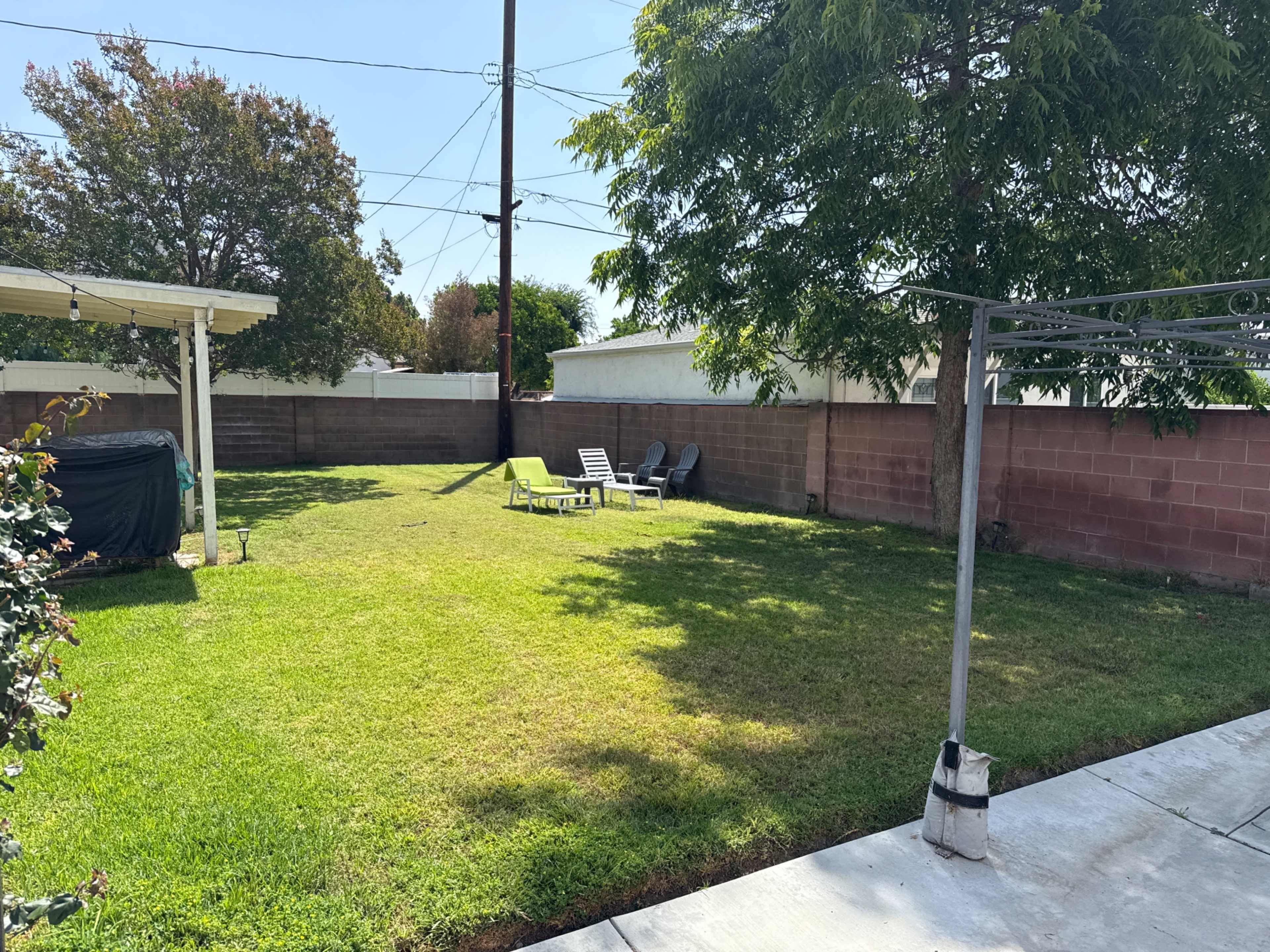 The image shows a grassy backyard with a few lounge chairs and a clothesline, bordered by a low brick wall.