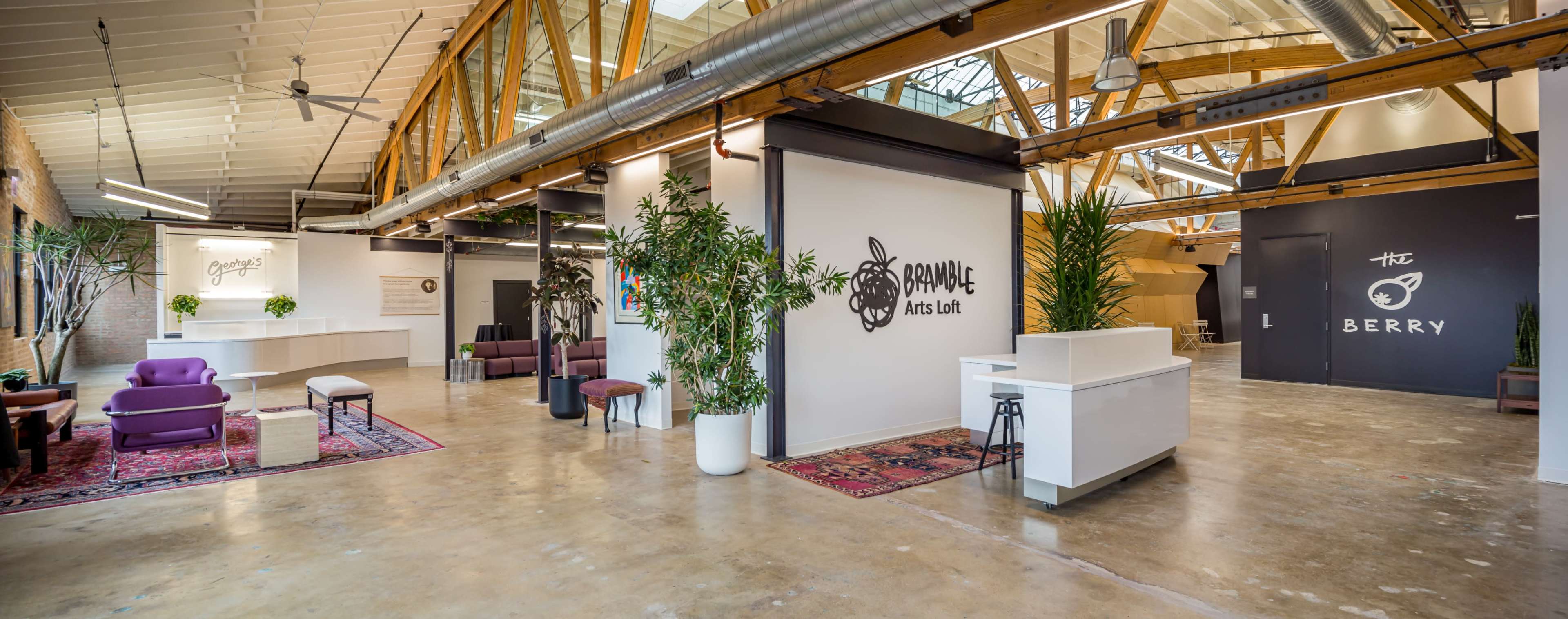 A spacious arts loft with high wooden beams, distinct areas for seating, and a reception space featuring plants and artwork against white walls.