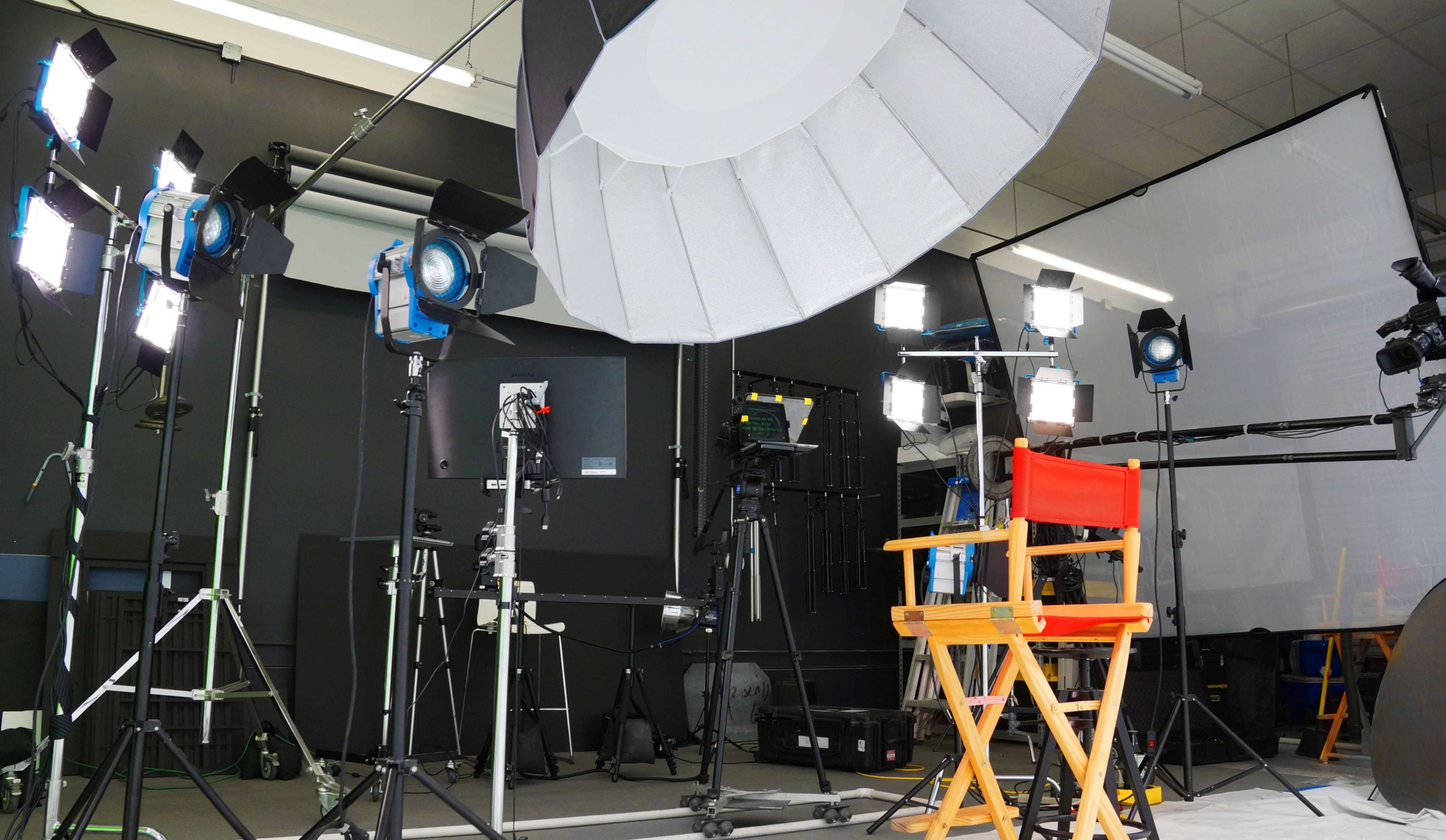 A film set with a red director's chair in front of various lighting equipment and backdrops.