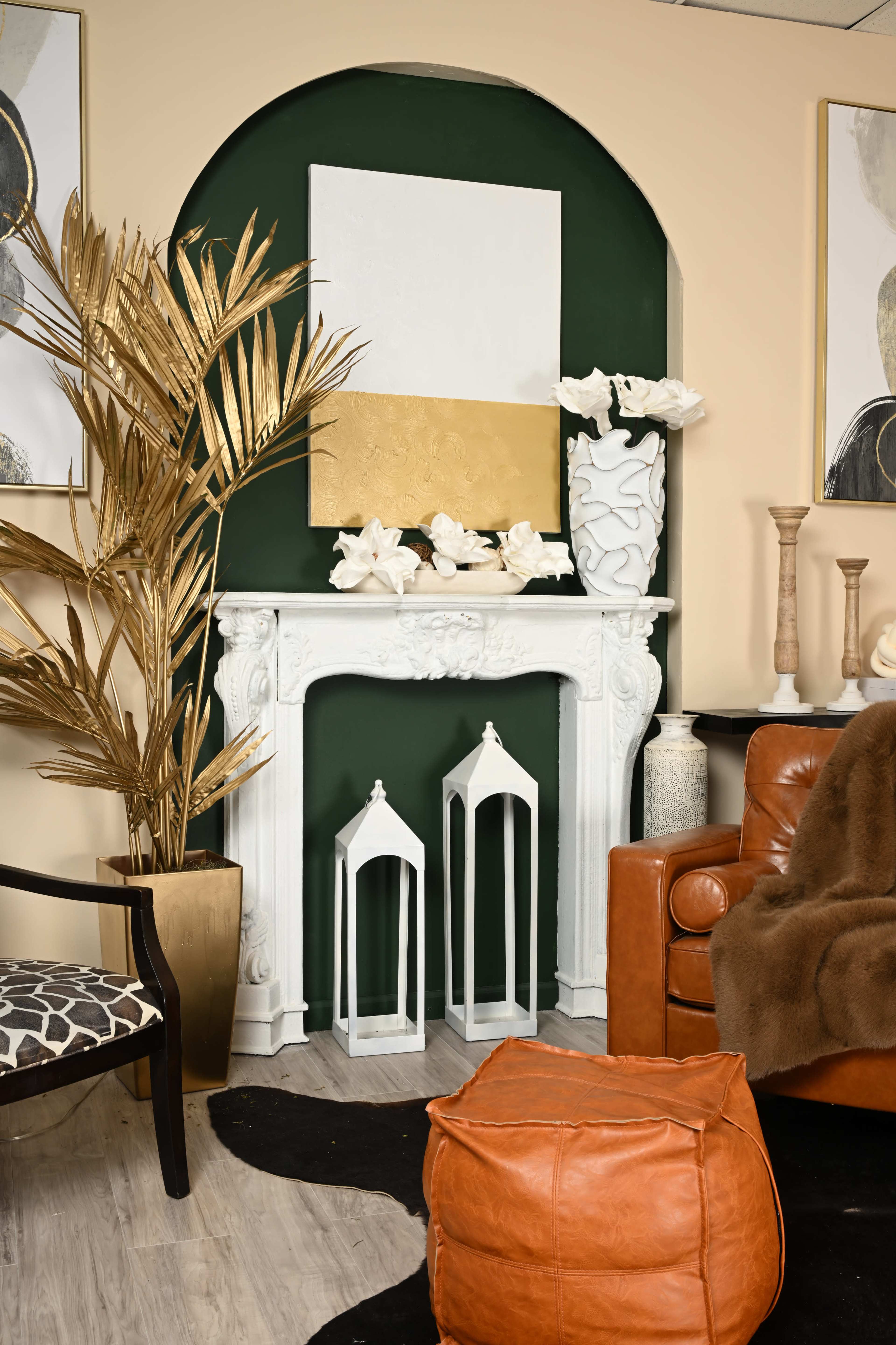 The image features a stylish interior with a green archway above a white fireplace, adorned with decorative items, including a large gold plant, white flowers, and various vases, accompanied by a brown leather chair and an orange pouf.