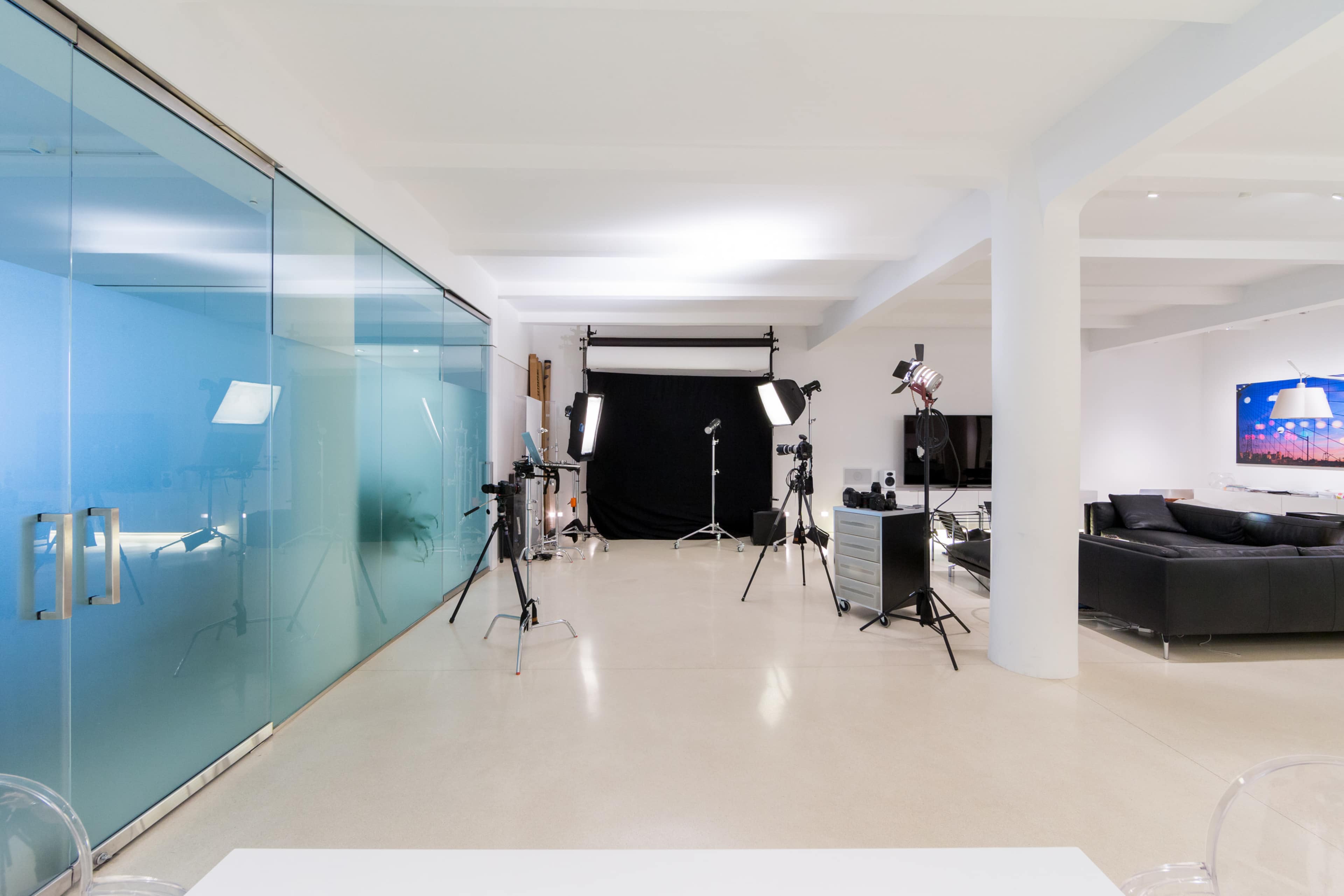 A spacious studio features a glass-walled area and various lighting equipment set up against a black backdrop.